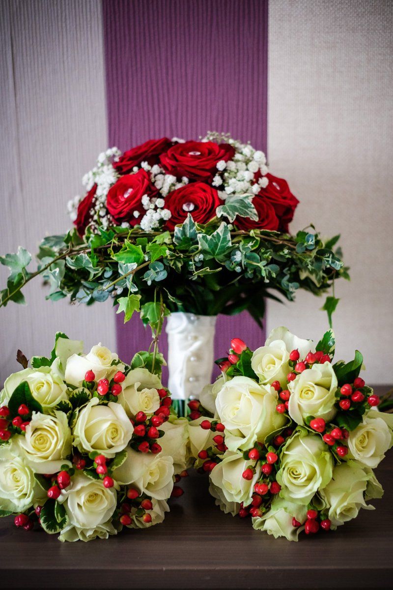 Wedding bouquets: red roses with greenery, white roses with red berries.