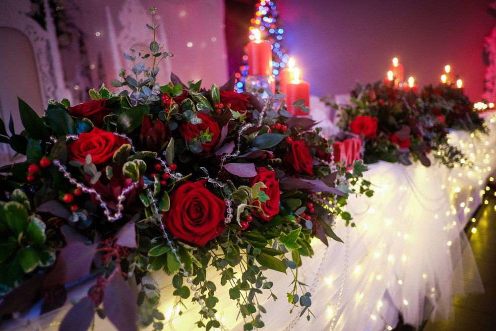 Red roses and greenery table centerpiece with candles and fairy lights.