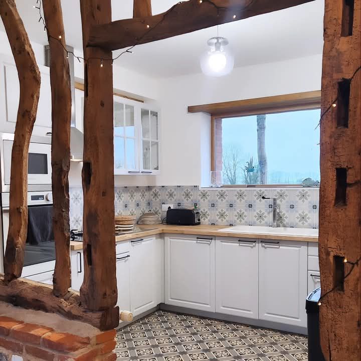 Une cuisine avec des armoires blanches et des poutres en bois à Fécamp en Normandie