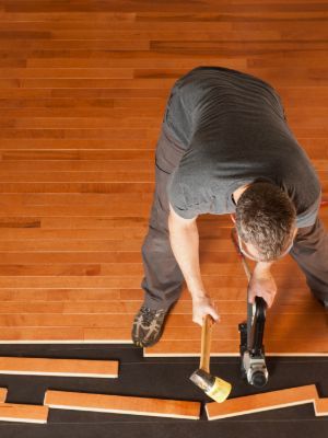 A man is working on a wooden floor with a hammer.