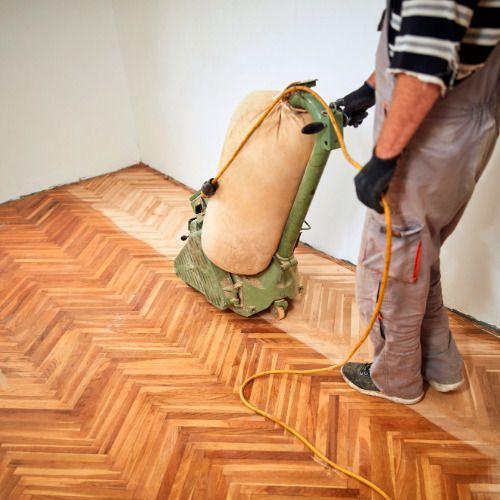 A man is sanding a wooden floor with a machine.