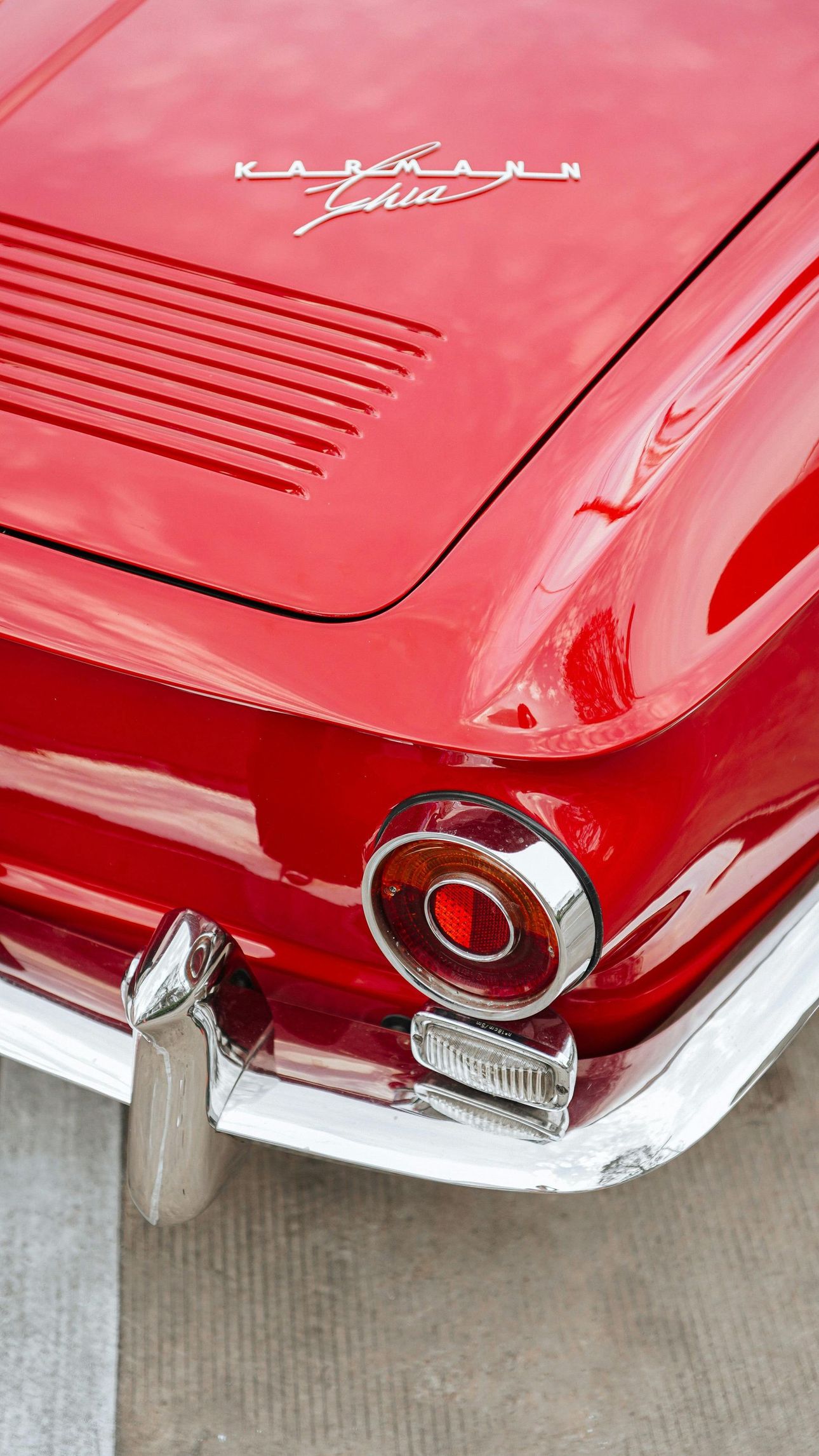 Red vintage Karmann Ghia car rear detail, chrome accents, and taillight.