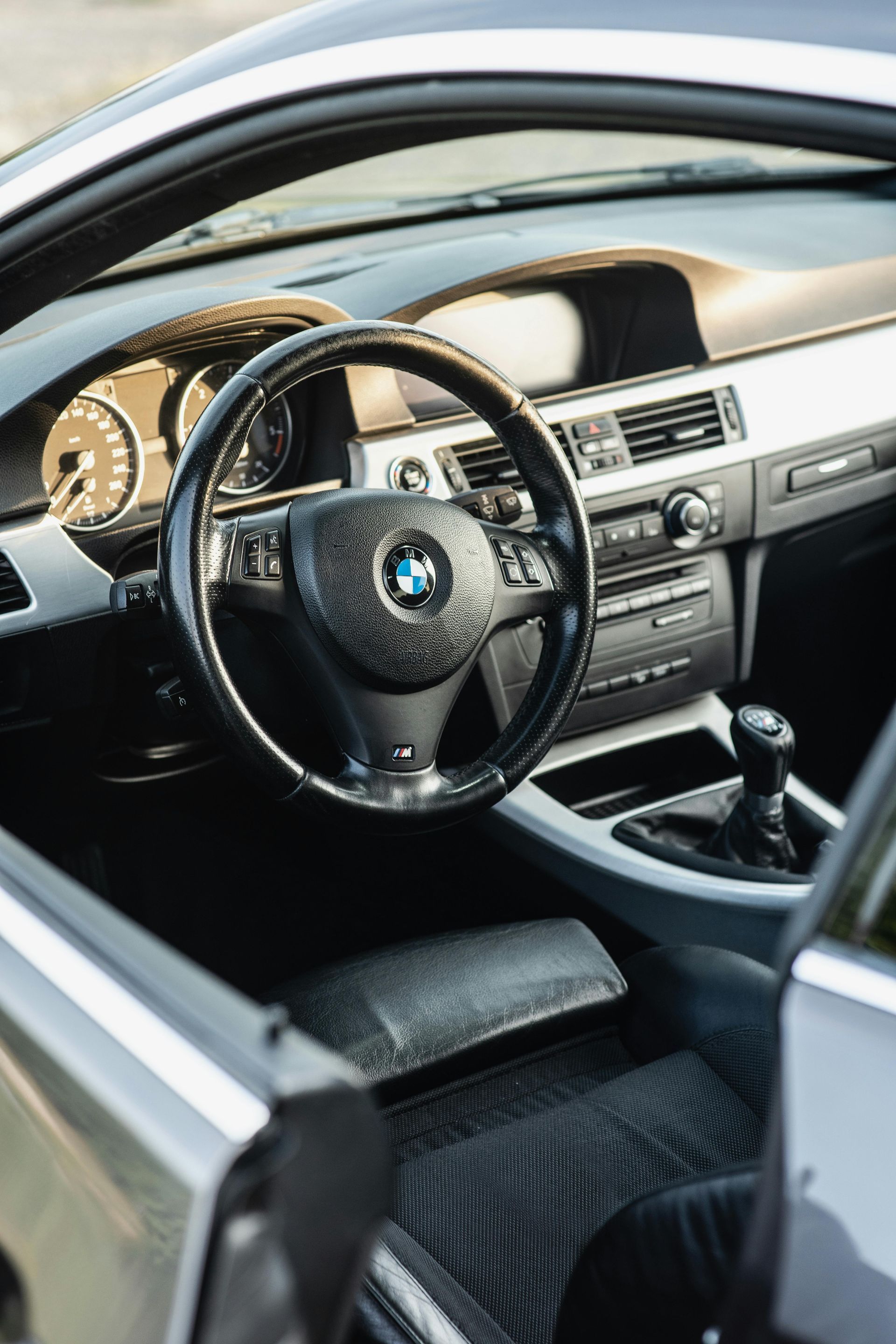 Interior of a black BMW car: steering wheel, dashboard, gear shift, and driver's seat.