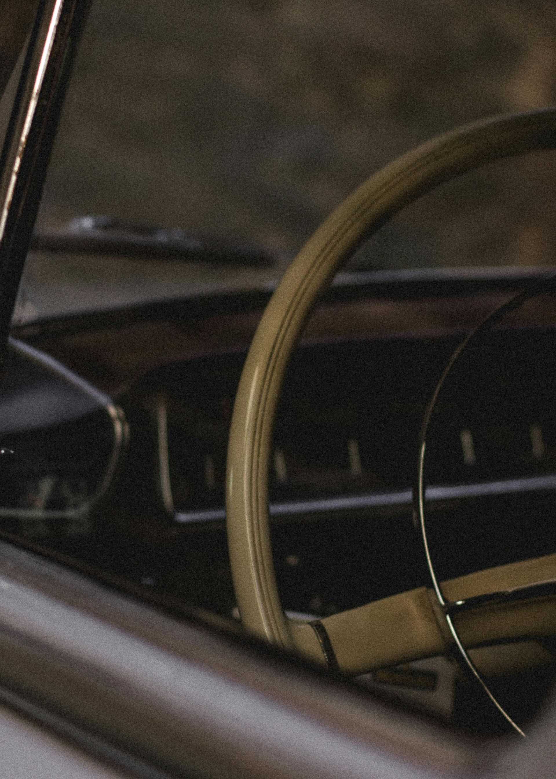 Steering wheel inside an old car, cream-colored with dark dashboard and outside view.