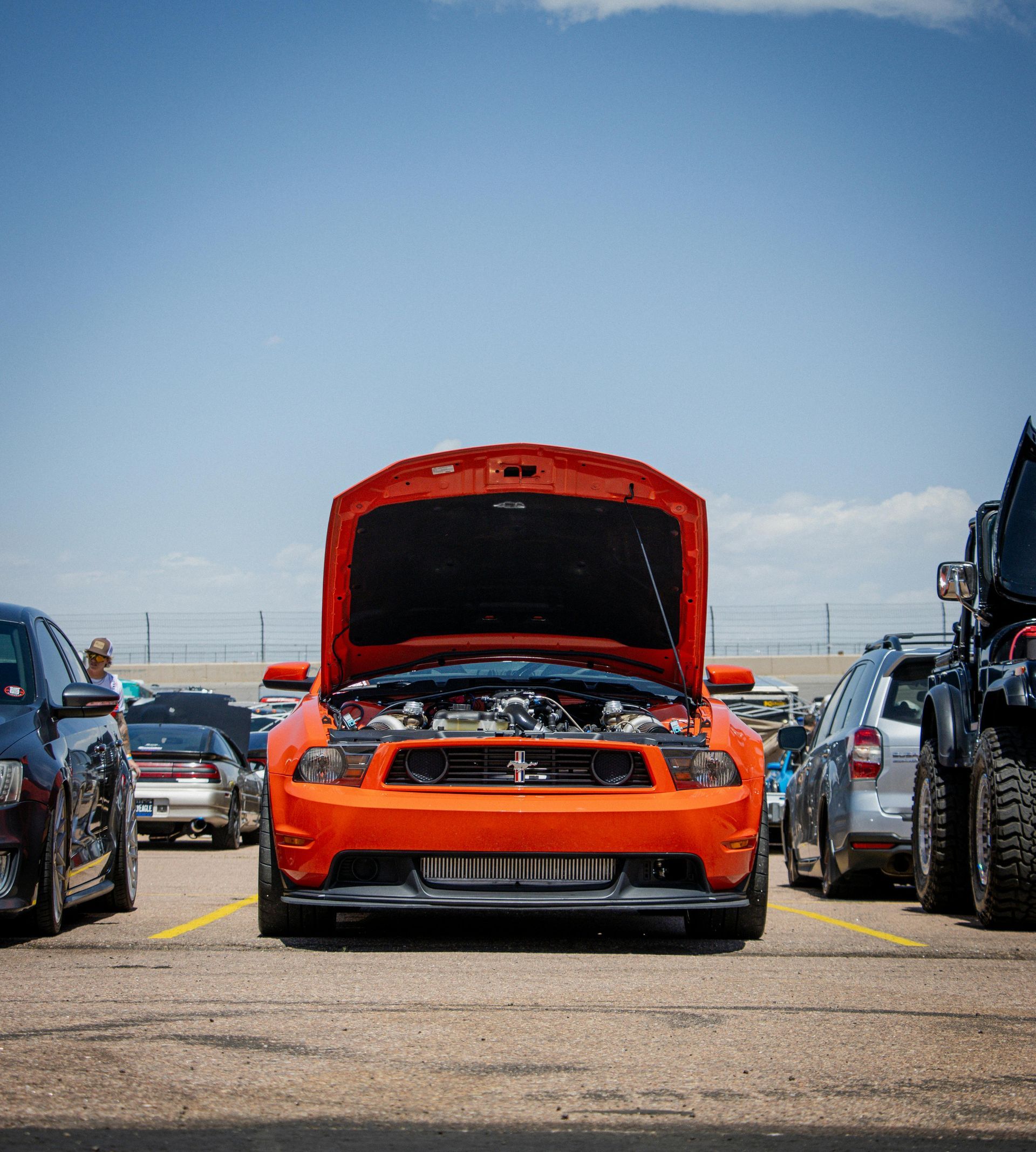 Orange Mustang with open hood at a car show.