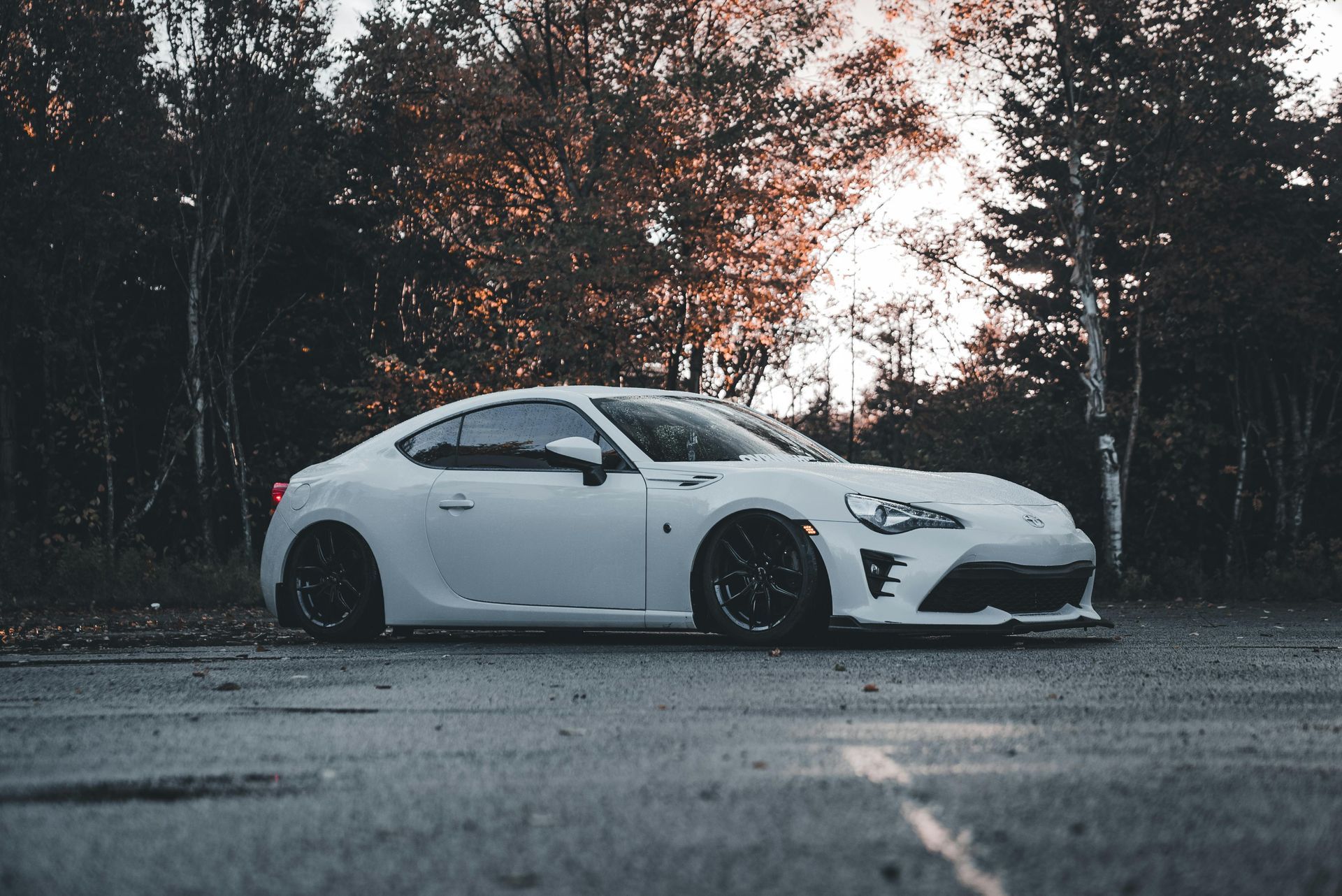 White sports car parked on a road, surrounded by trees.