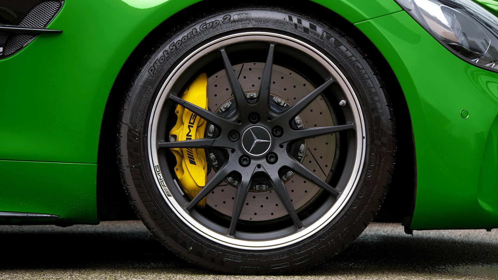 Green Mercedes-Benz car wheel with black rim, yellow brake caliper, and silver accents.