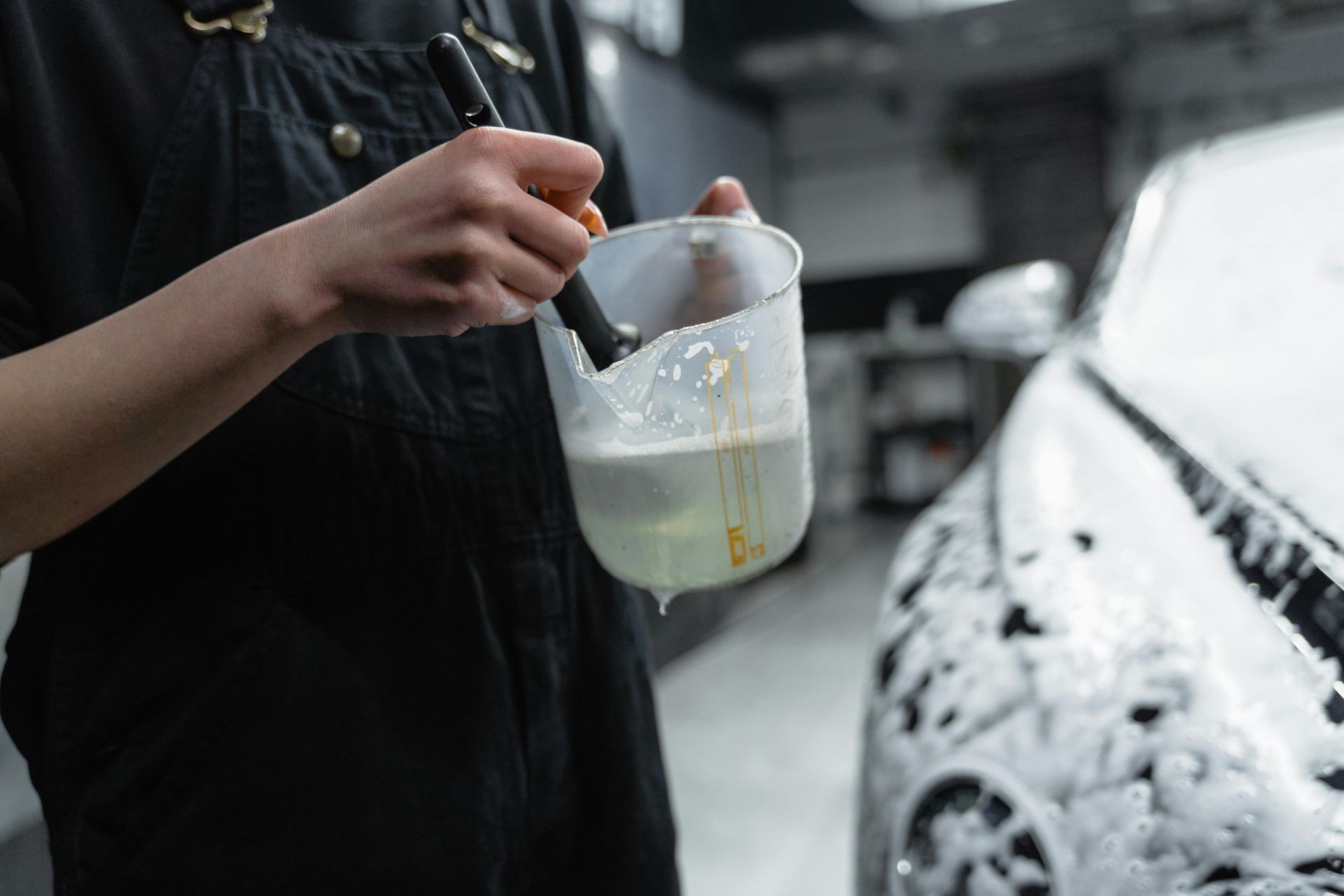 Person cleaning a car with a brush and soapy water in a container.