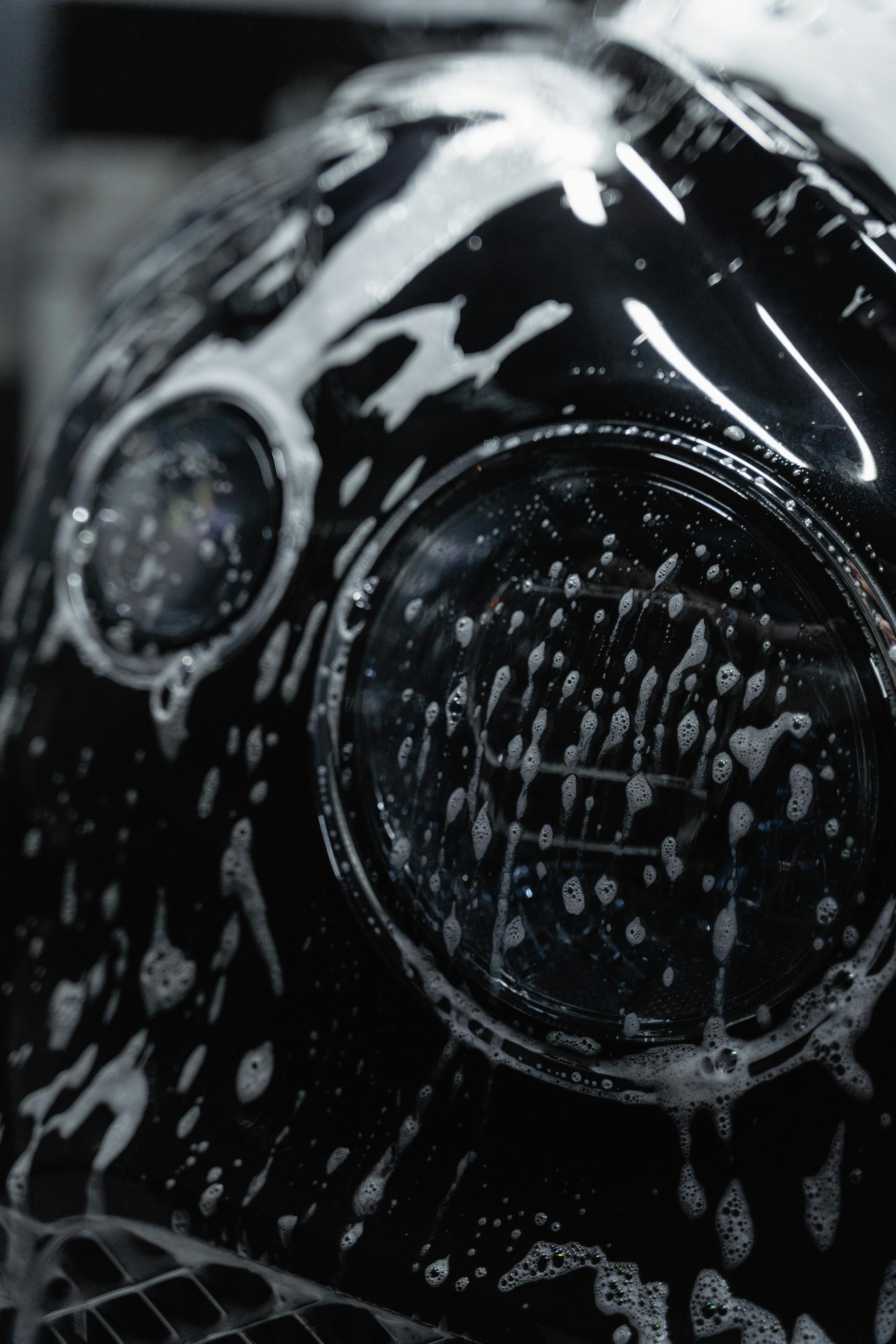 Black vehicle headlight covered in white soapy water.