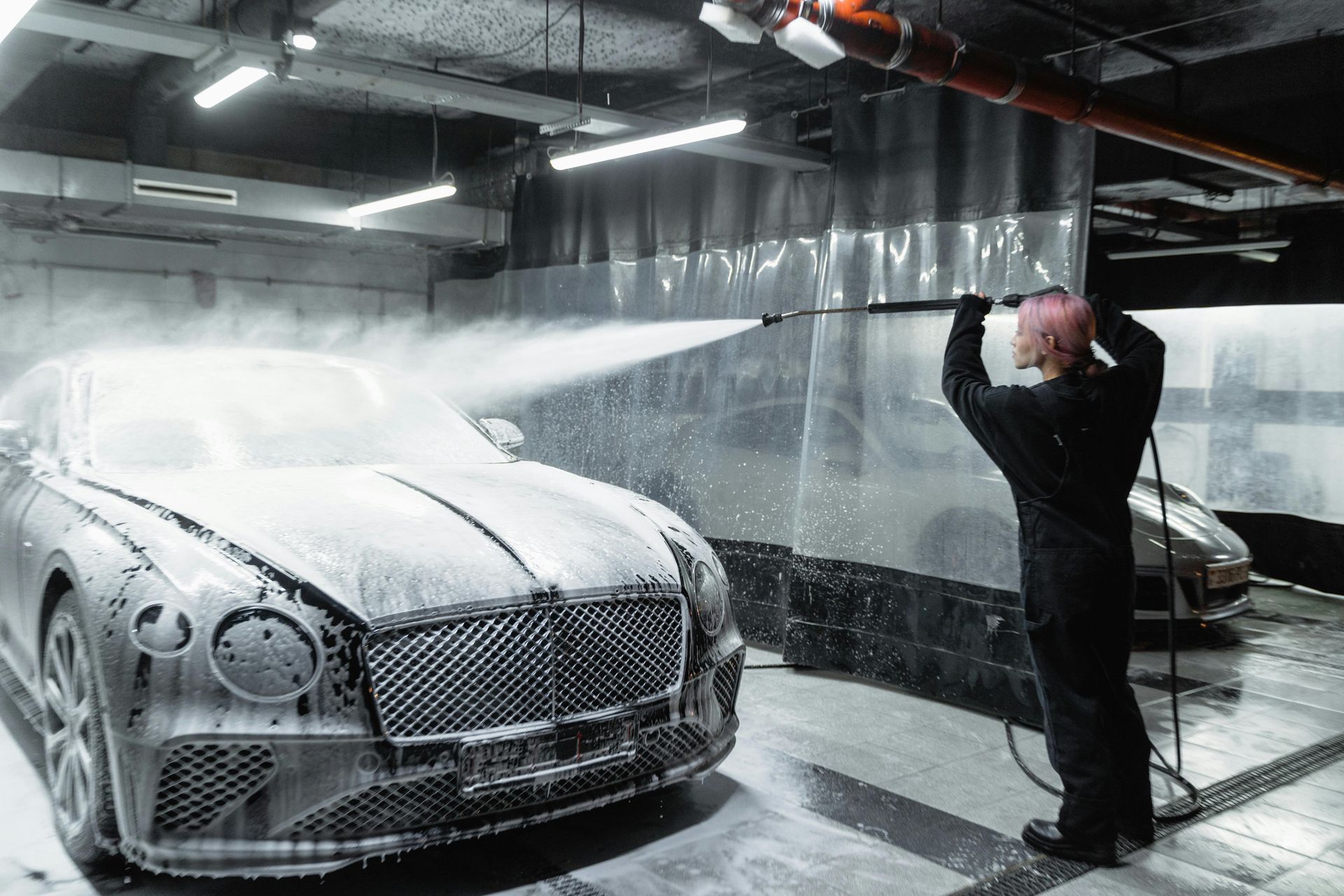 Person washes a silver Bentley with foamy soap in a garage.