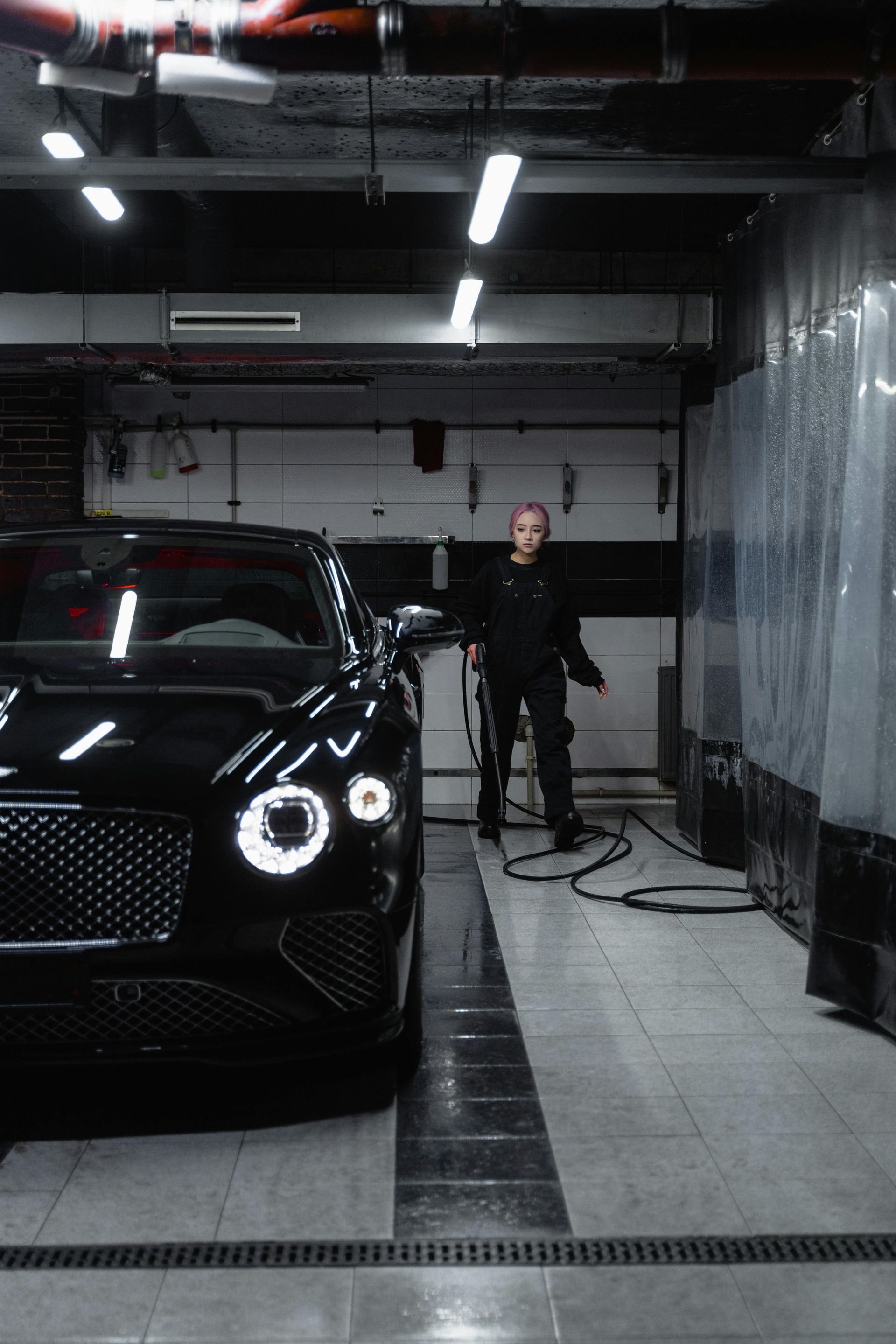 A woman in black stands in a car wash next to a black Bentley.
