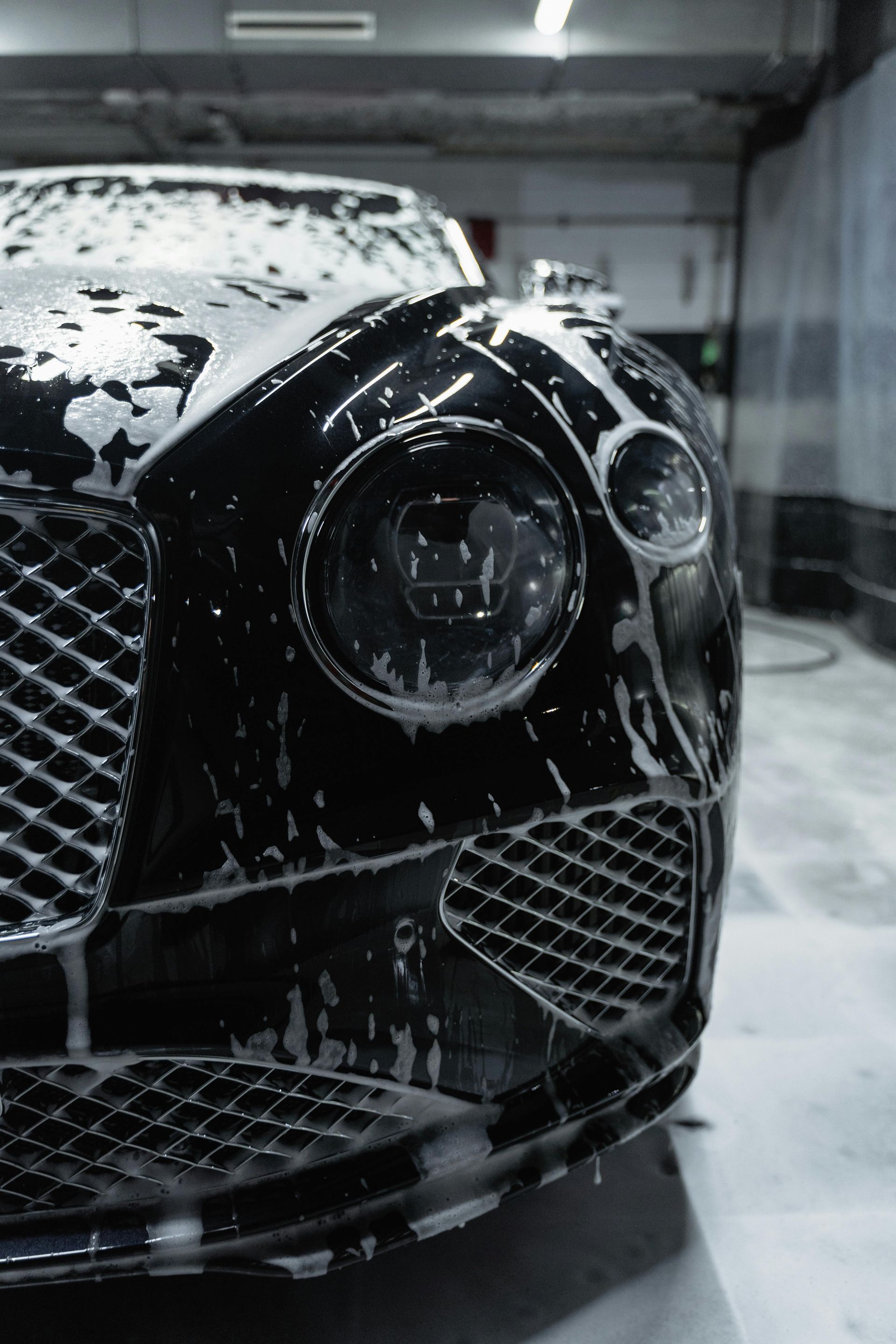Black Bentley covered in soap suds during a car wash.