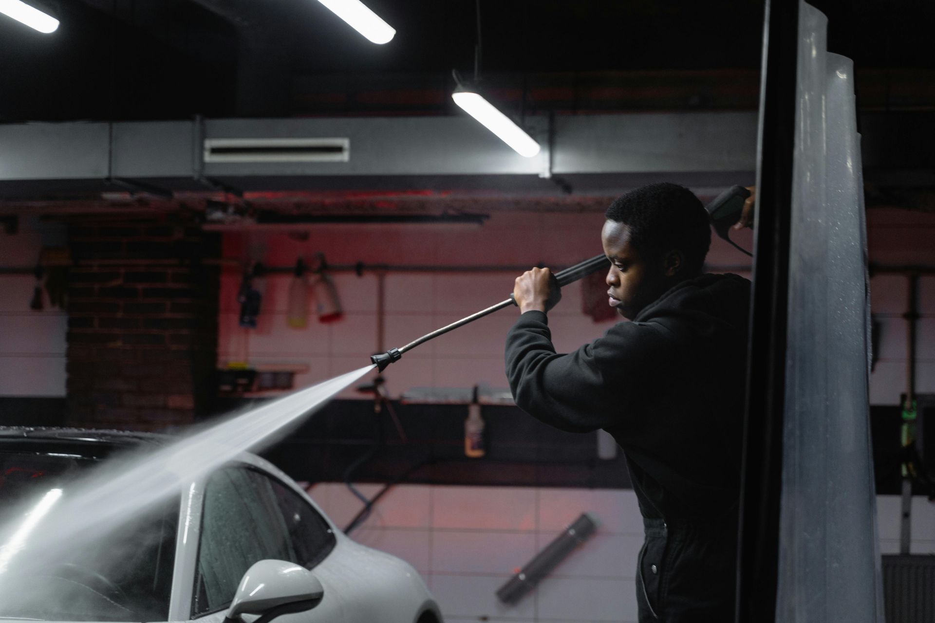 Man washing a white car with a pressure washer in a car wash bay.