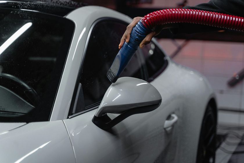 White car being dried with a blue and red hose in a garage.