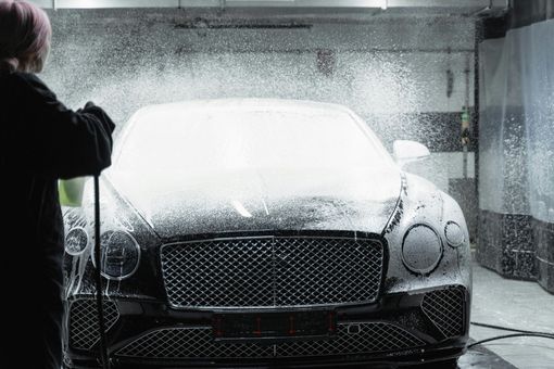 Person spraying a black Bentley with soapy water at a car wash.