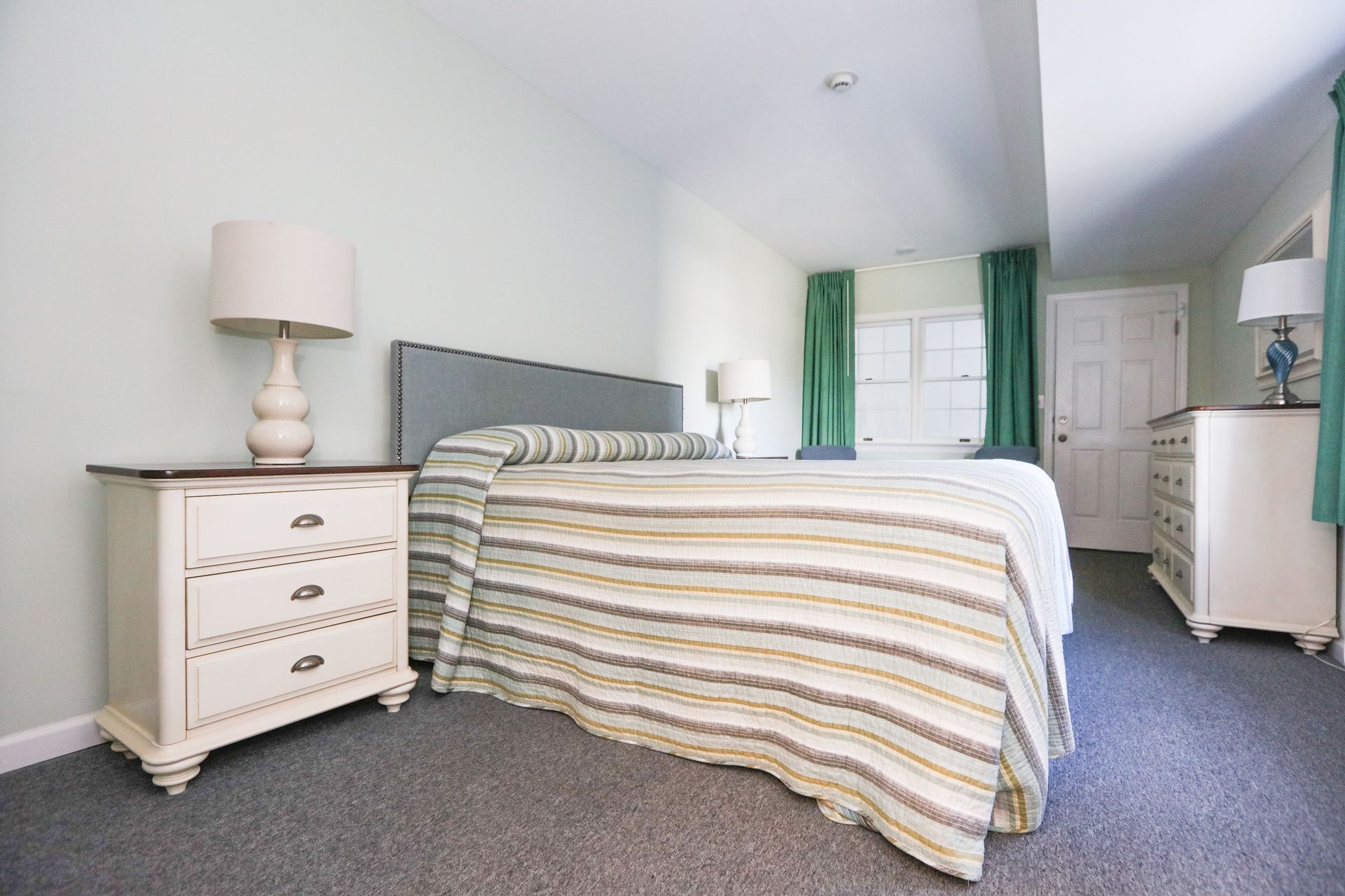 A bedroom with a bed , nightstand , lamp and dresser.