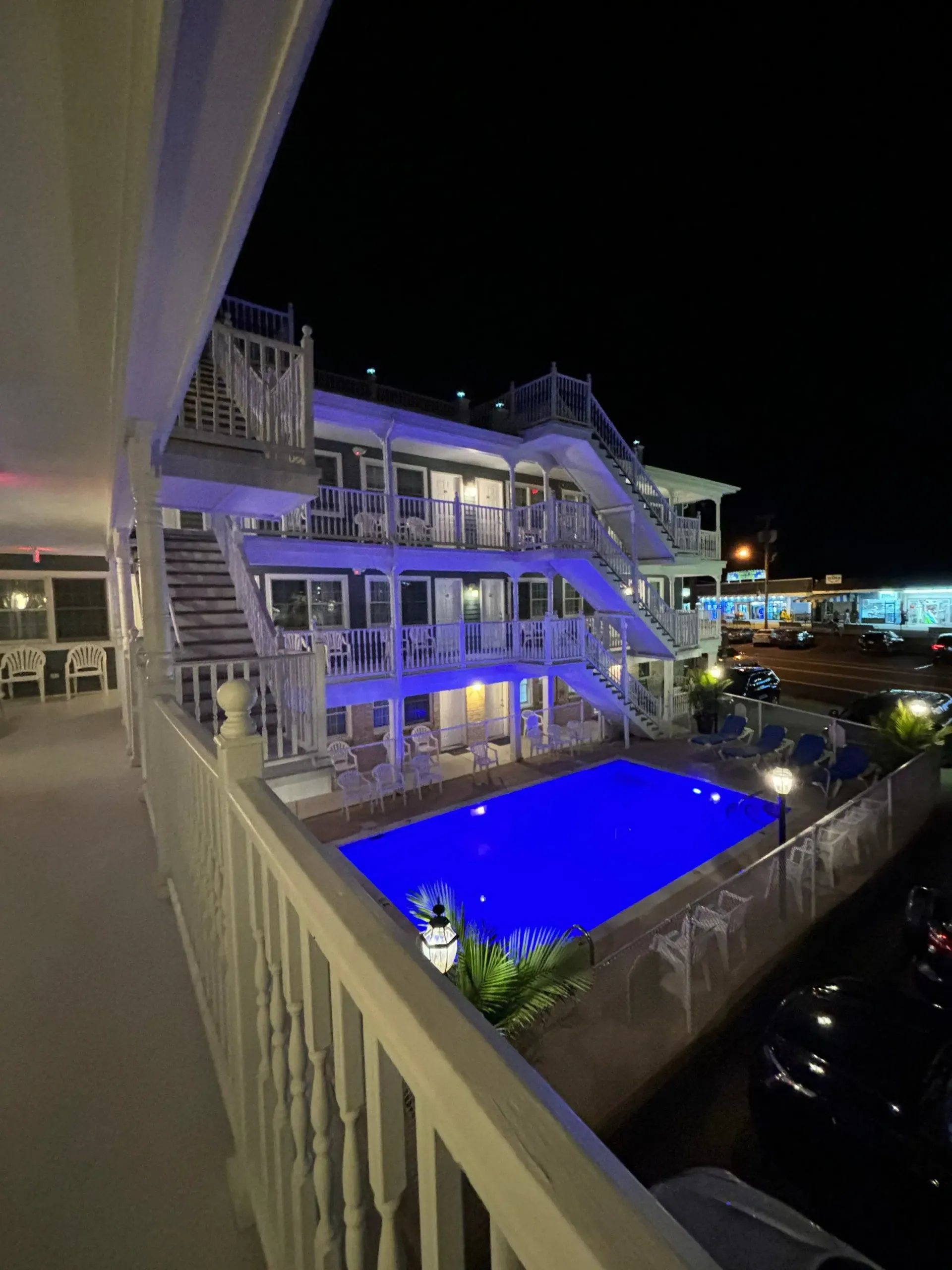 A large swimming pool is lit up at night in front of a hotel.