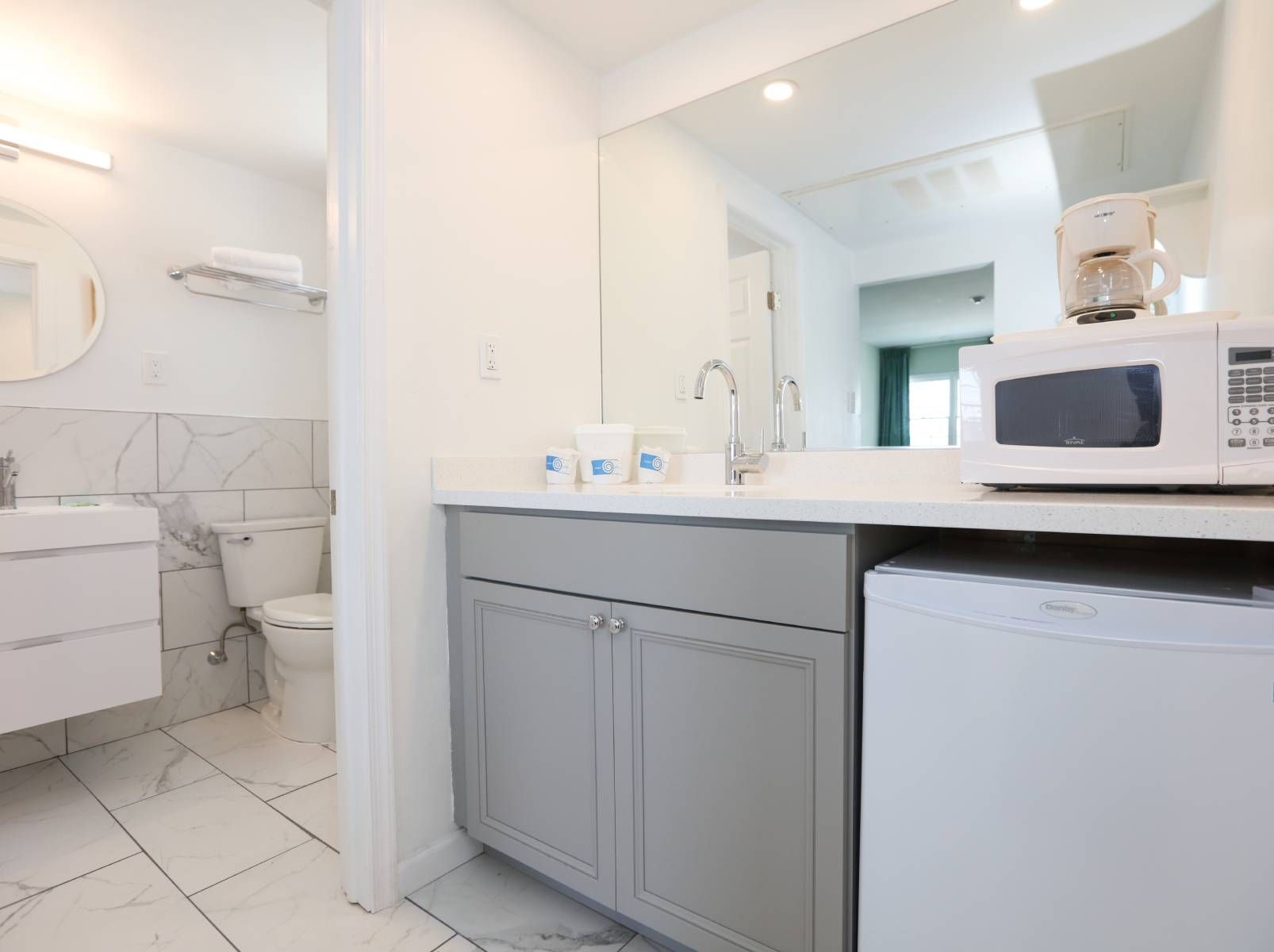 A bathroom with a sink , toilet , microwave and refrigerator.