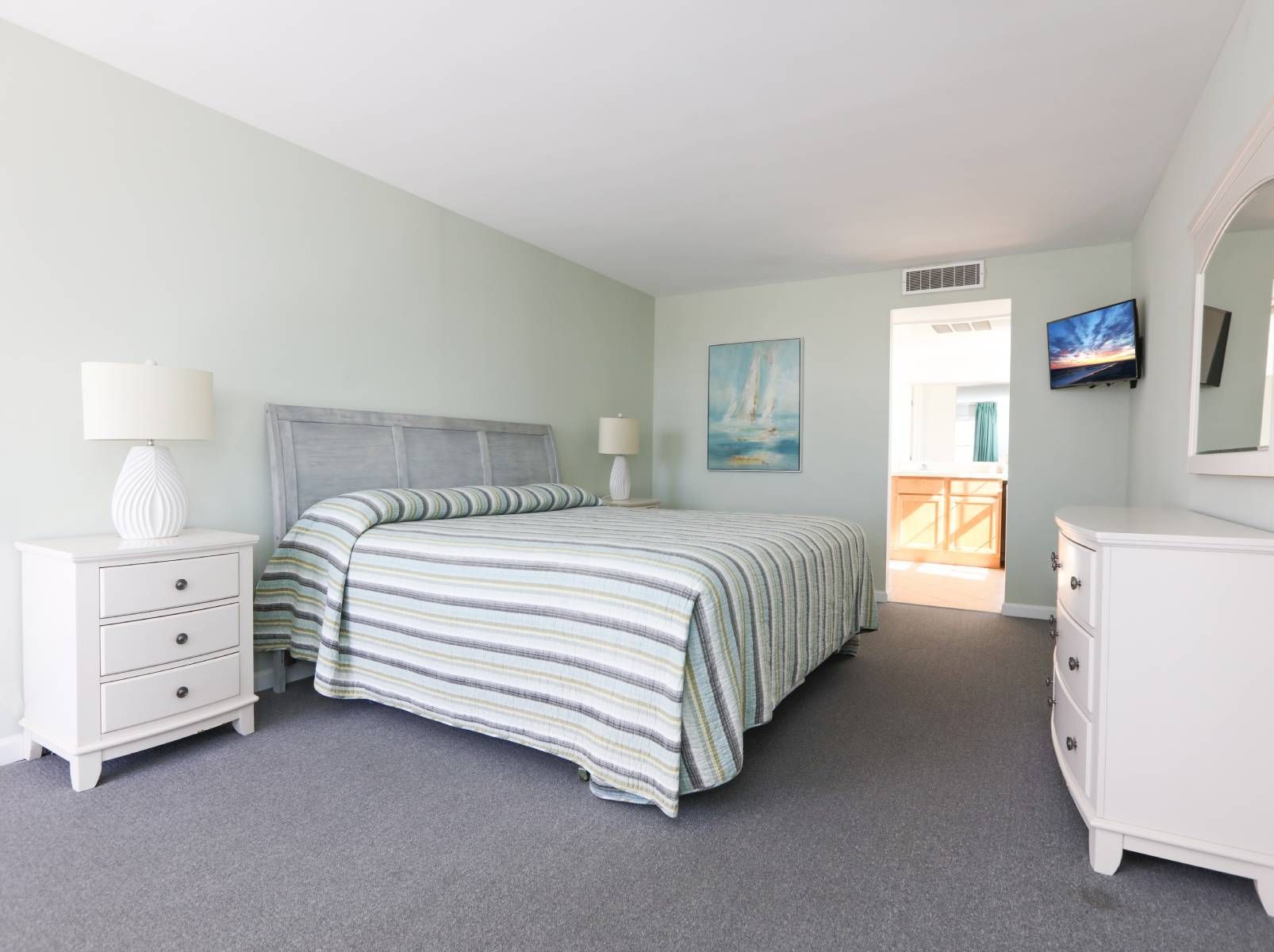 A bedroom with a king size bed , dresser , nightstand , mirror and television.