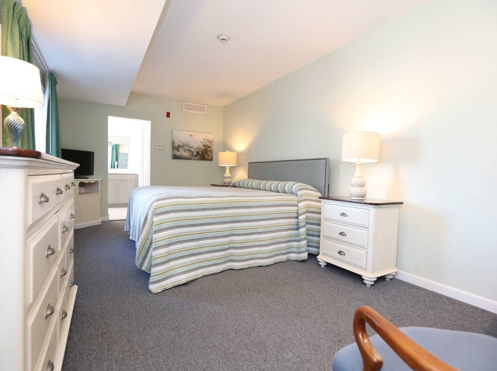 A bedroom with a large bed , dresser , nightstand and chair.