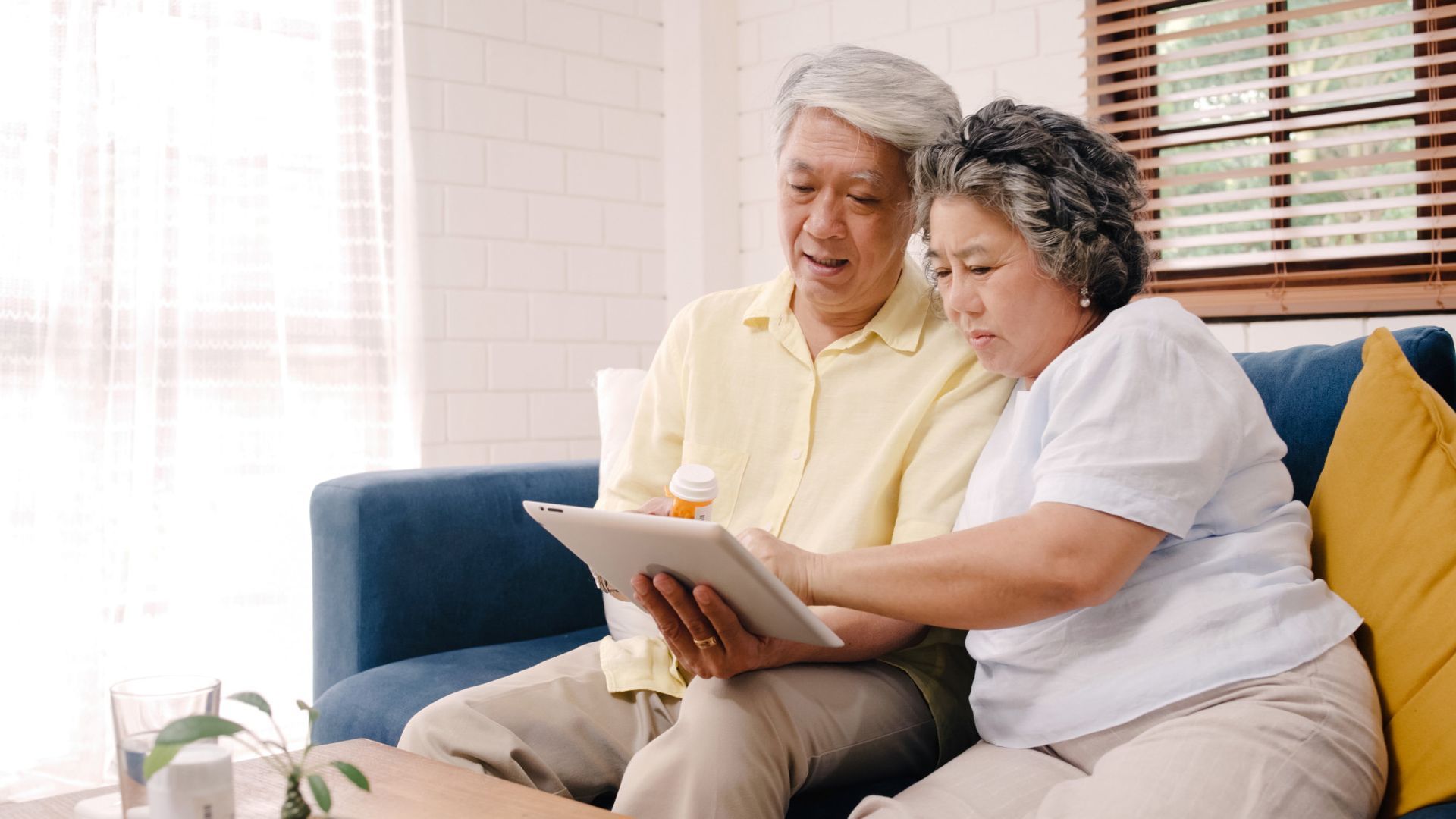 Senior couple using tablet on blue sofa; looking at screen.