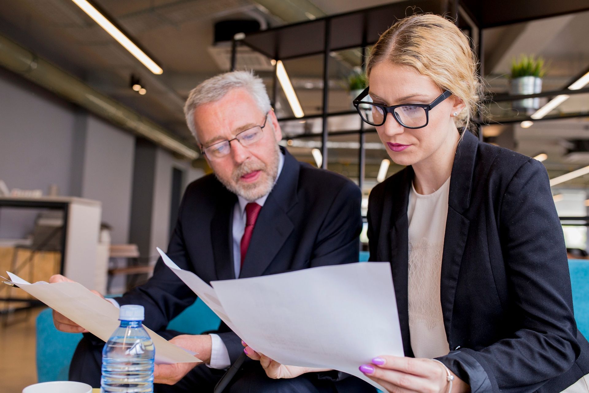 Man and woman in business attire reviewing documents, indoors.