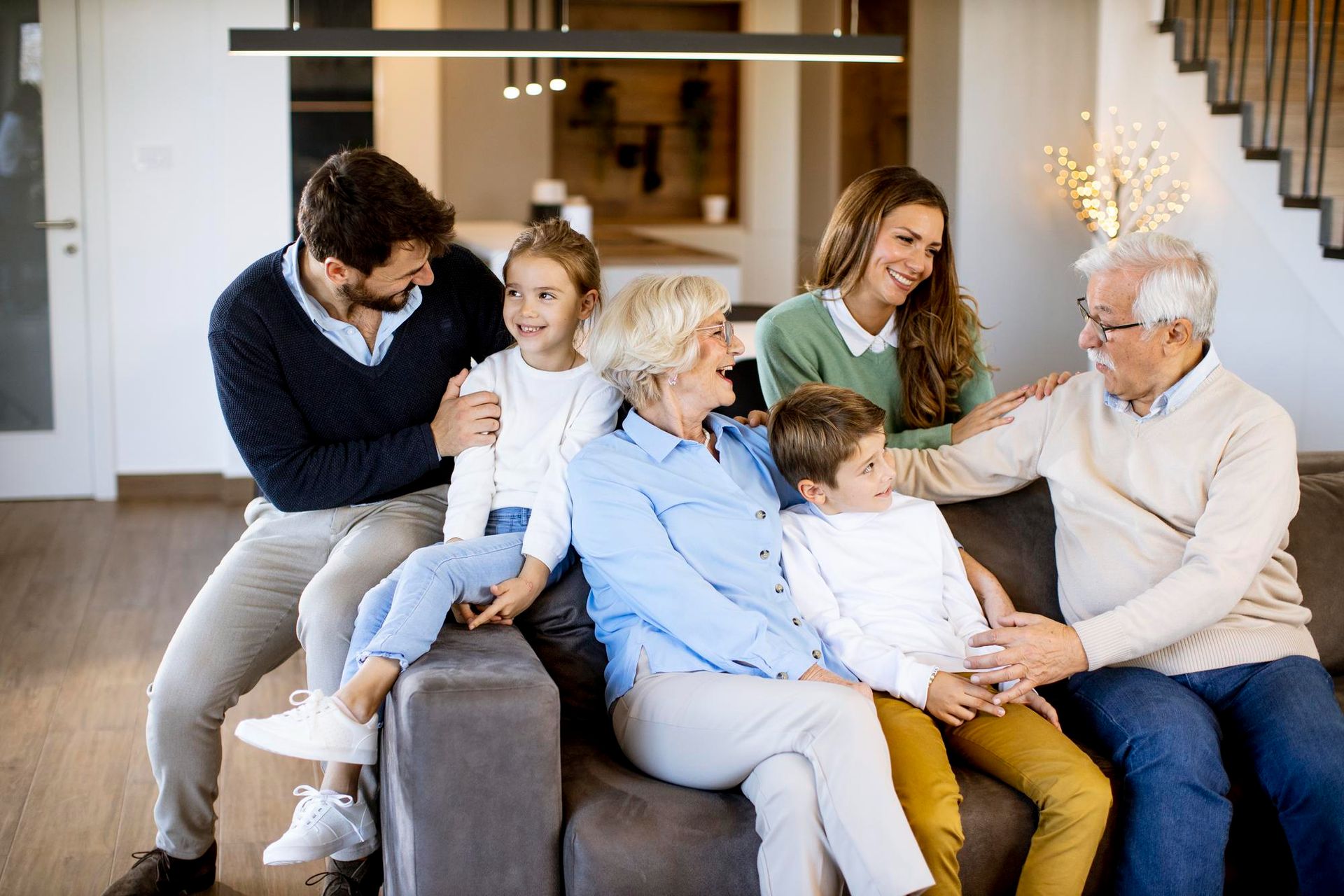 Family of seven sitting on a sofa, smiling. Indoors, casual attire.