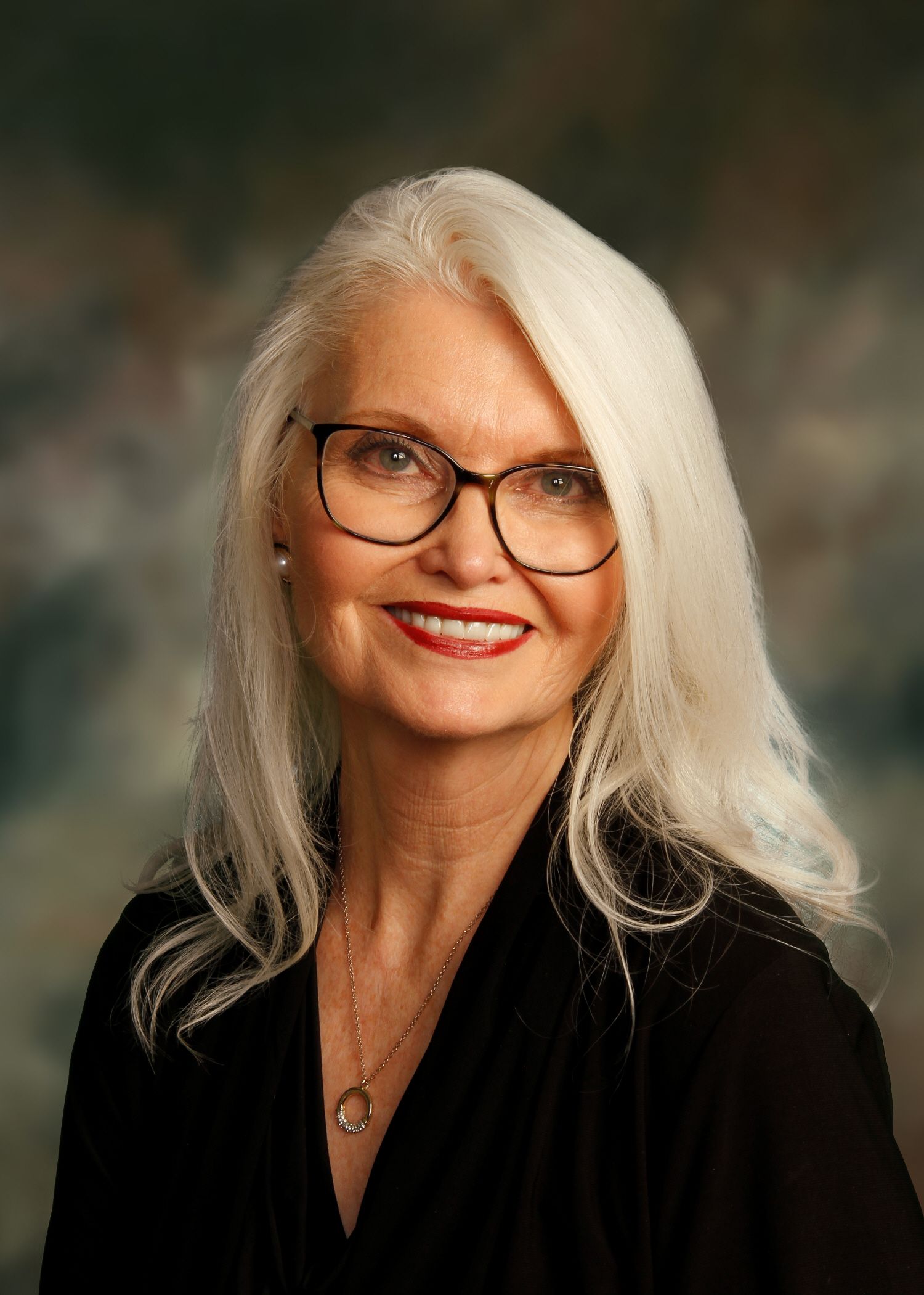 Woman with white hair, glasses, and red lipstick, wearing a black top, smiling.