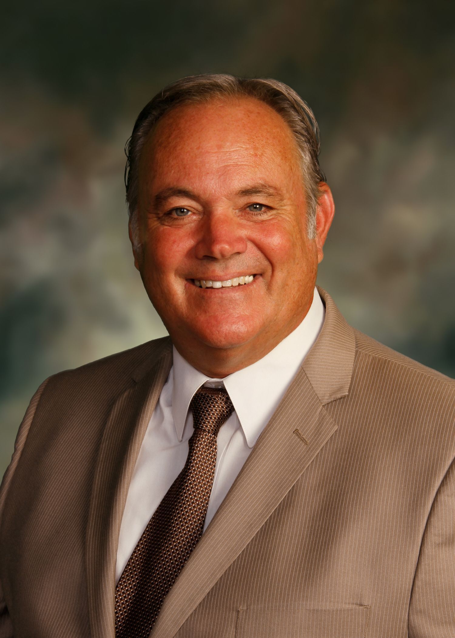 Man in a brown suit smiling at the camera.