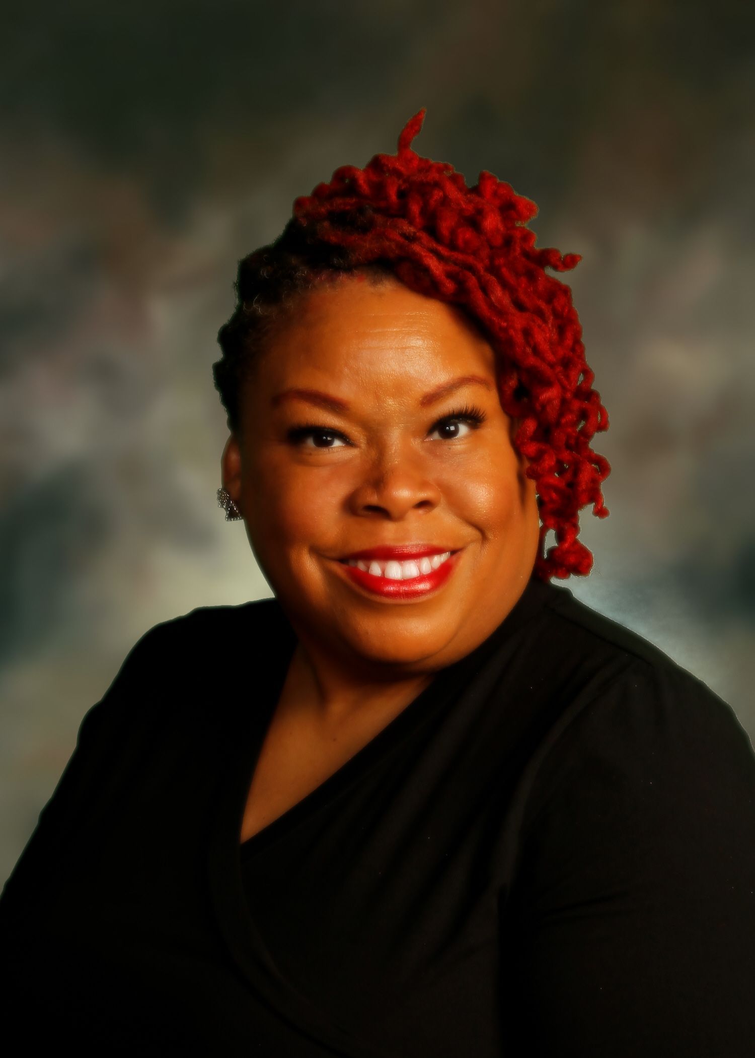 Woman with red dreadlocks smiles, wearing black top, against a blurry background.