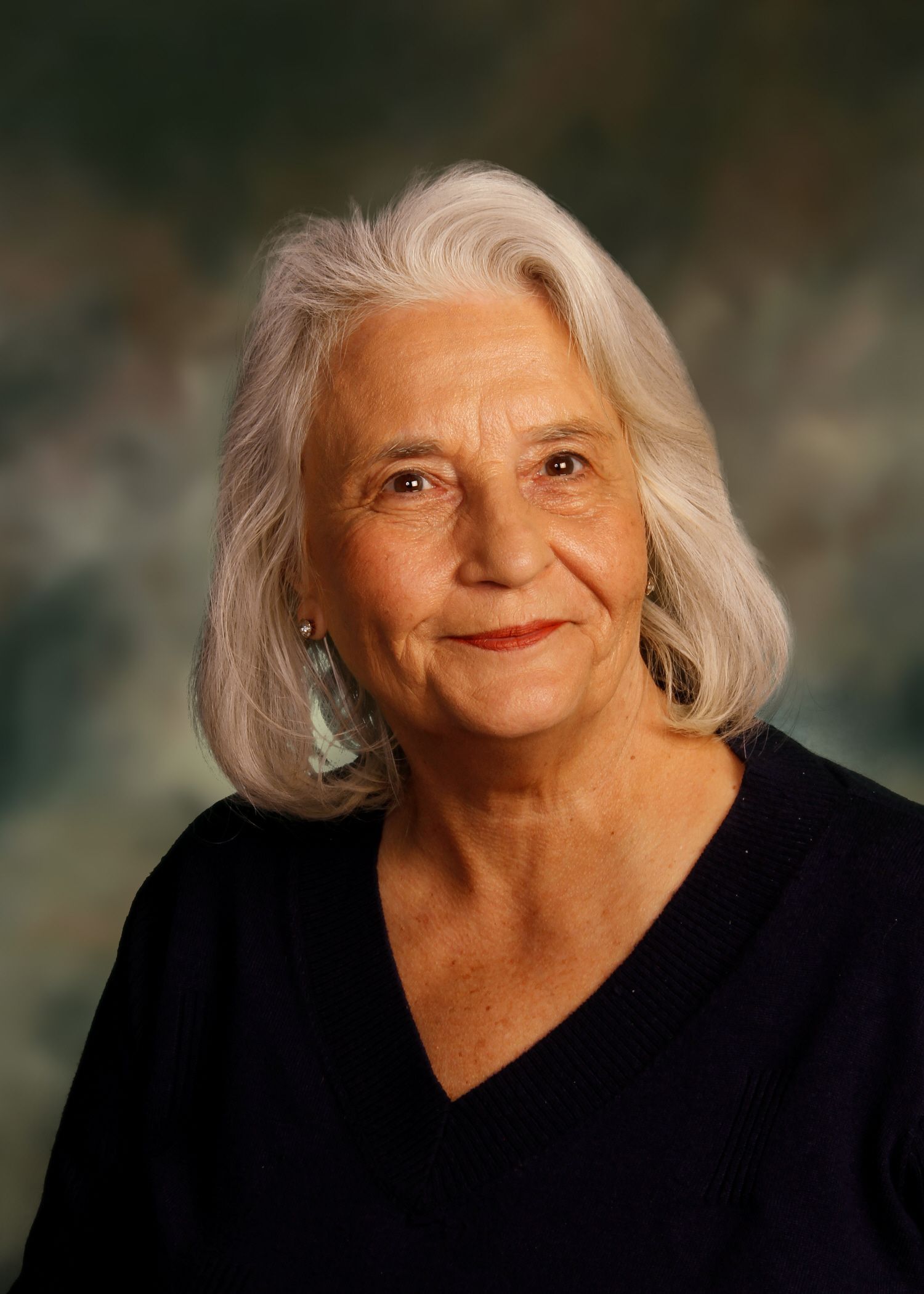 Elderly woman with white hair smiles, wearing a dark blue v-neck sweater.