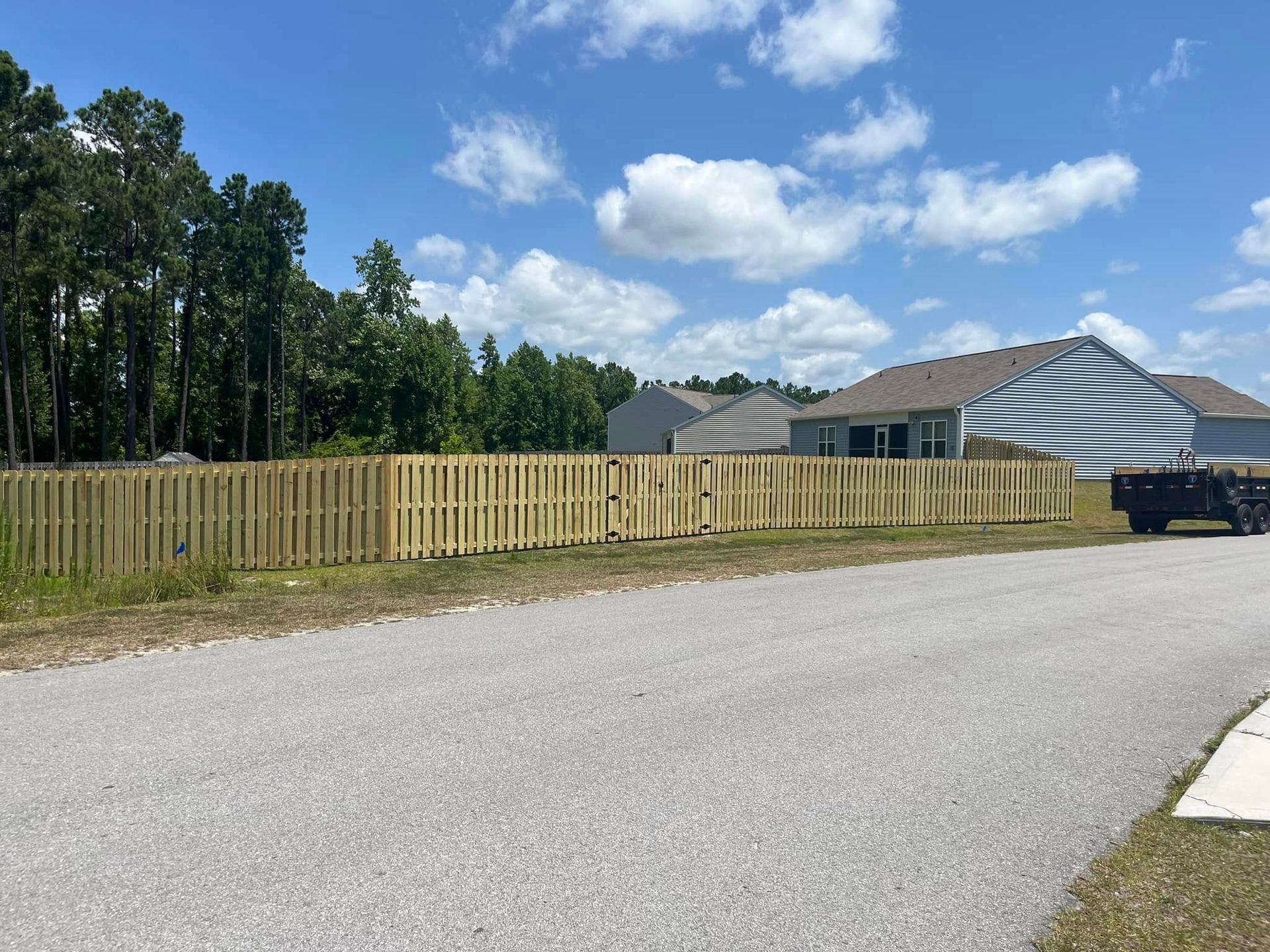 A truck is parked on the side of the road next to a wooden fence.