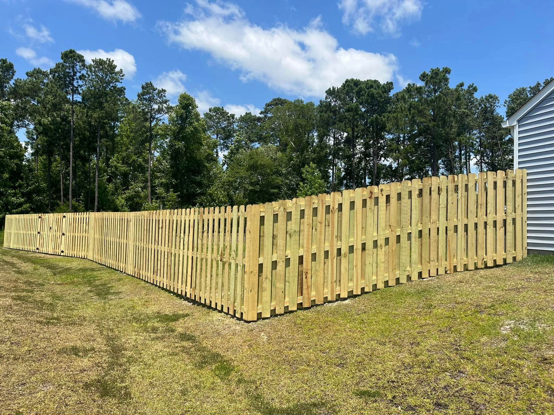 A wooden fence is in the middle of a grassy field in front of a house.