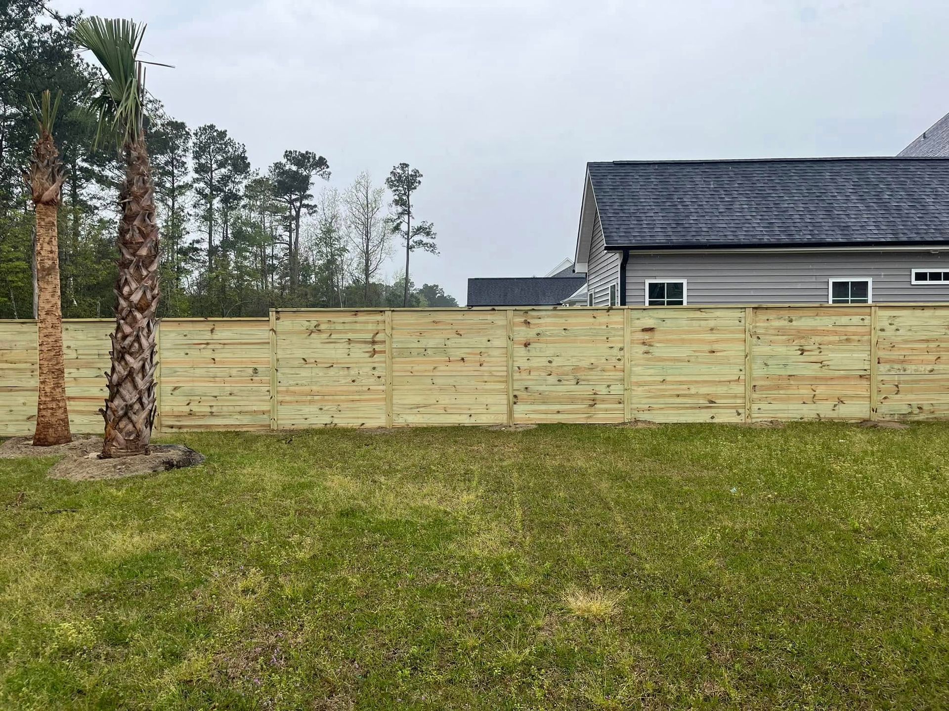 A wooden fence surrounds a lush green field in front of a house.