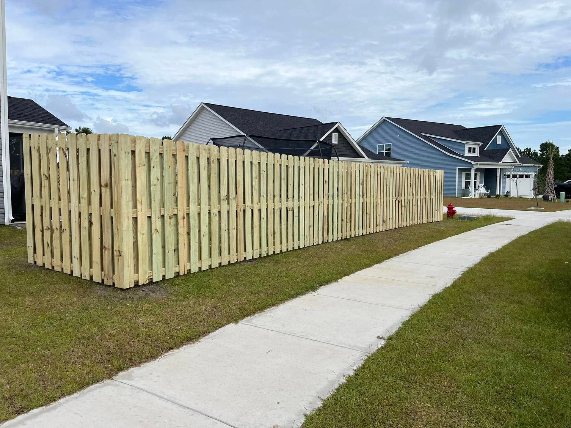 A wooden fence is sitting next to a sidewalk in front of a house.