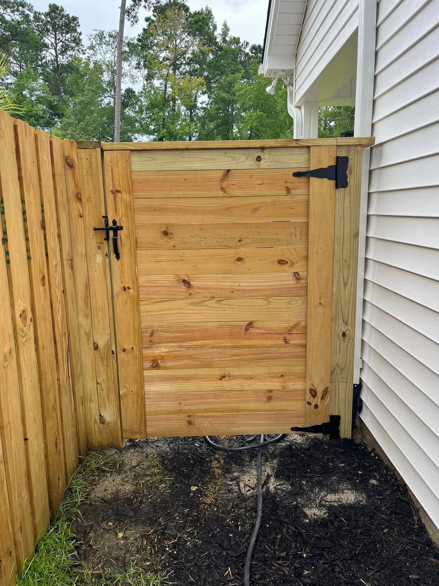 A wooden gate is attached to a wooden fence next to a house.