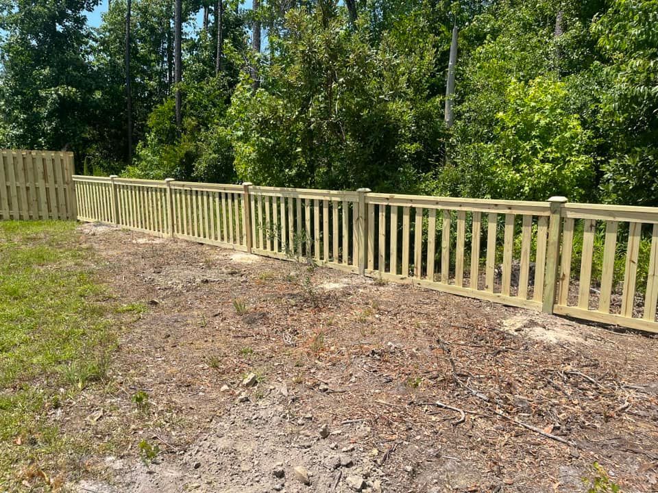 A wooden fence surrounds a dirt field with trees in the background.