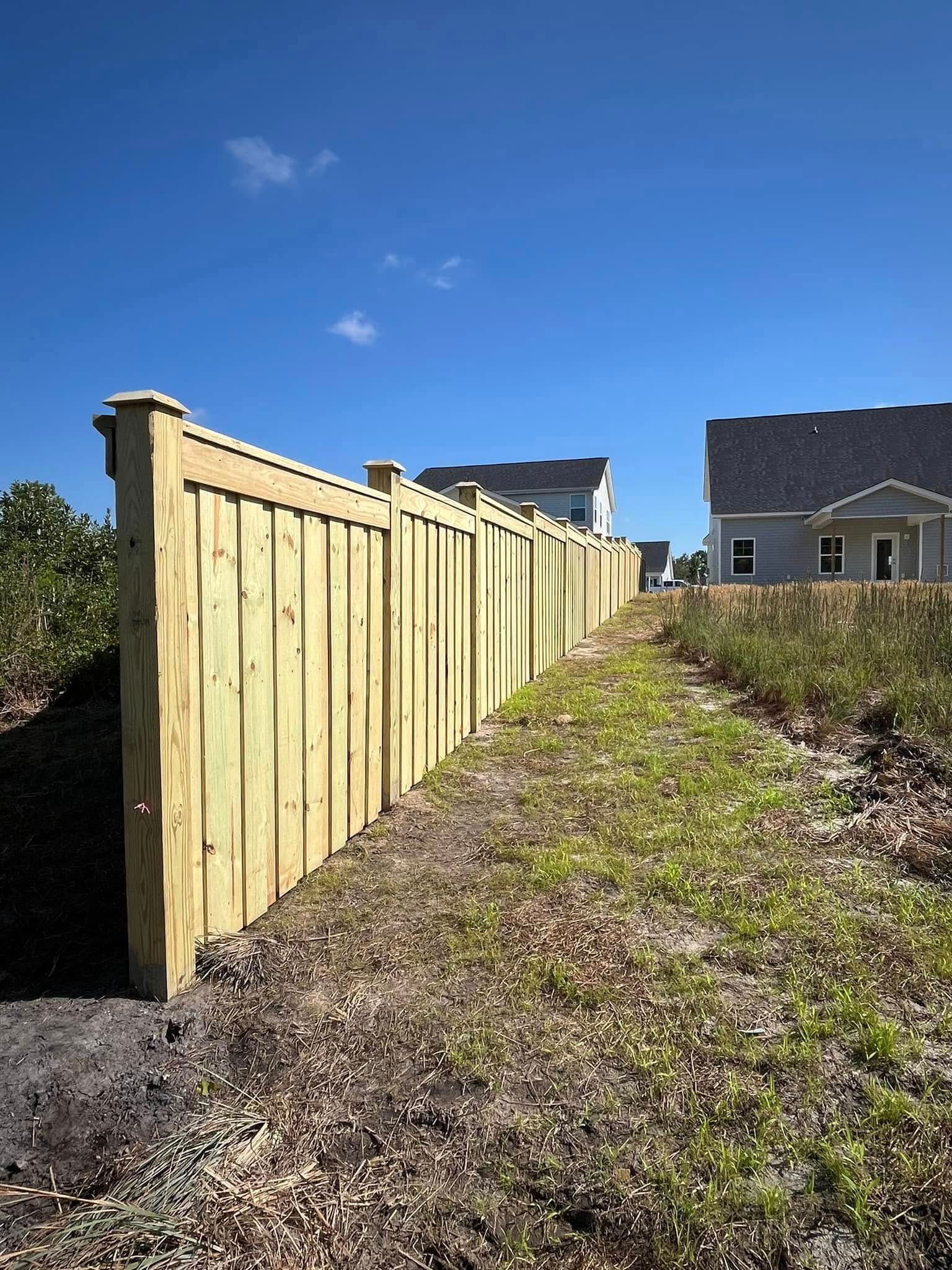 A wooden fence surrounds a grassy field next to a house.