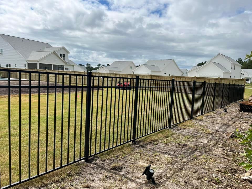 A black metal fence surrounds a lush green field.