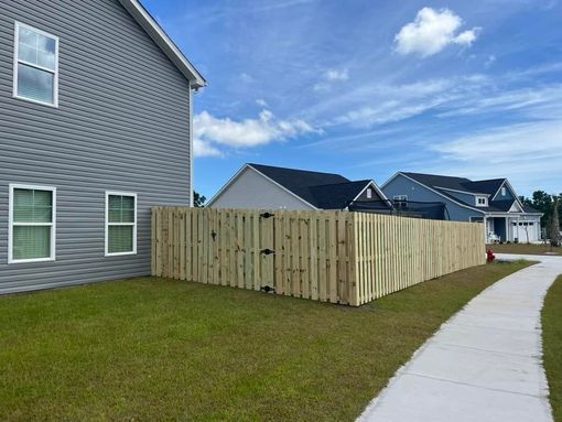 A wooden fence is in front of a house next to a sidewalk.