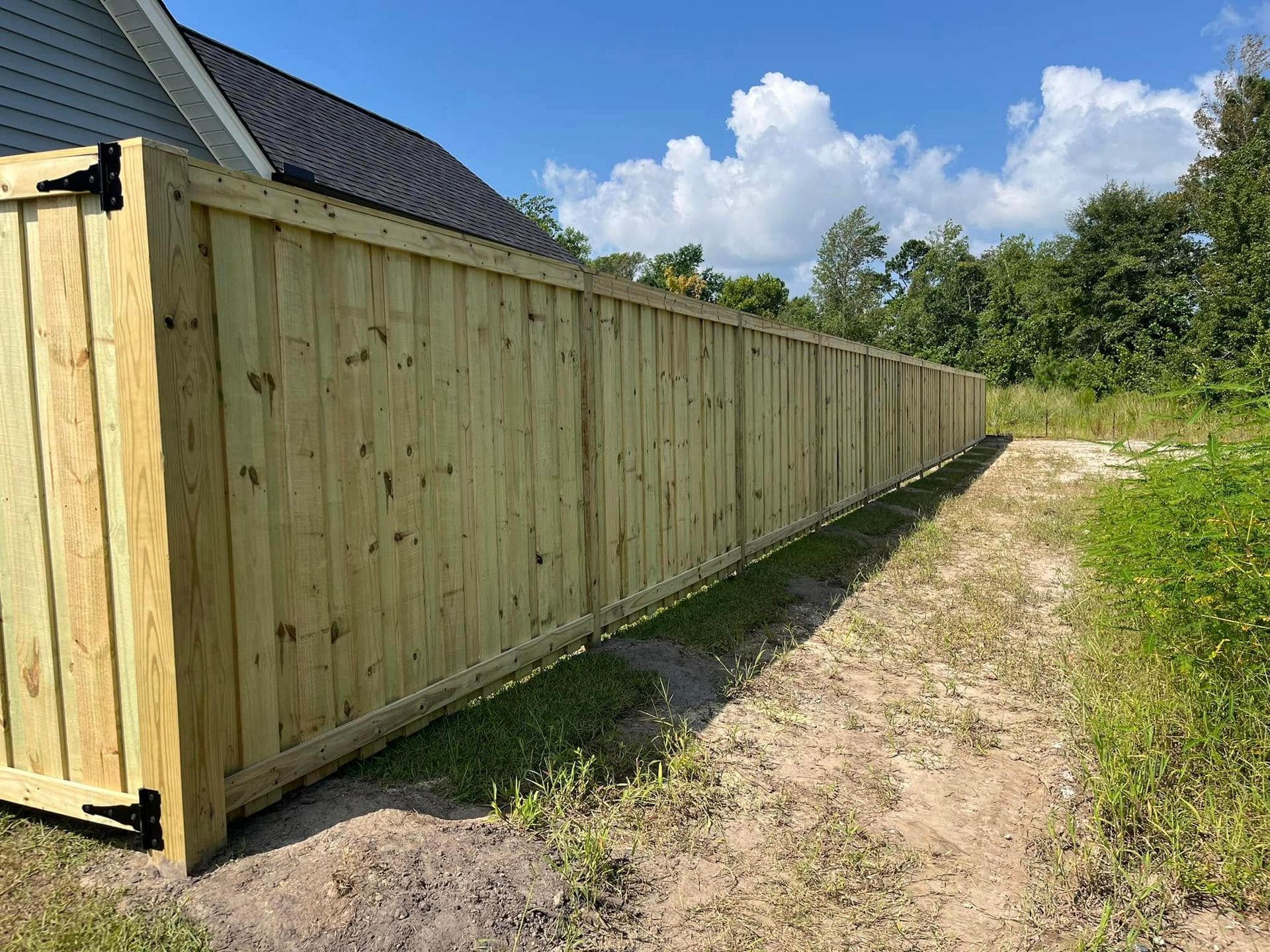 A long wooden fence is sitting next to a dirt road.