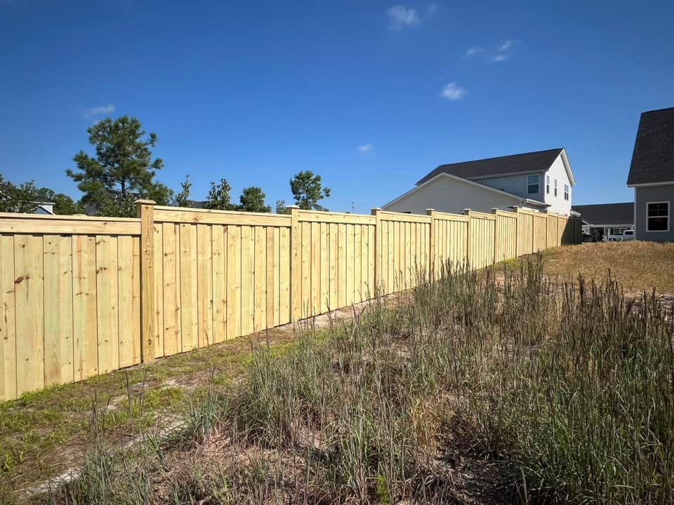 A wooden fence surrounds a grassy field in front of a house.