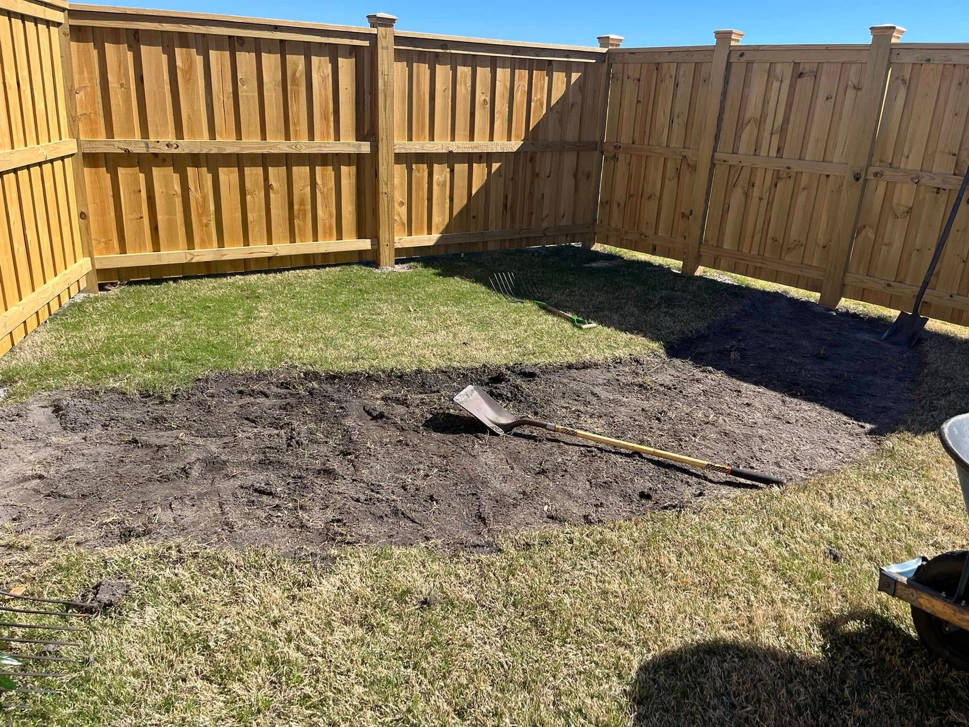 A wooden fence with a shovel in the dirt in front of it.