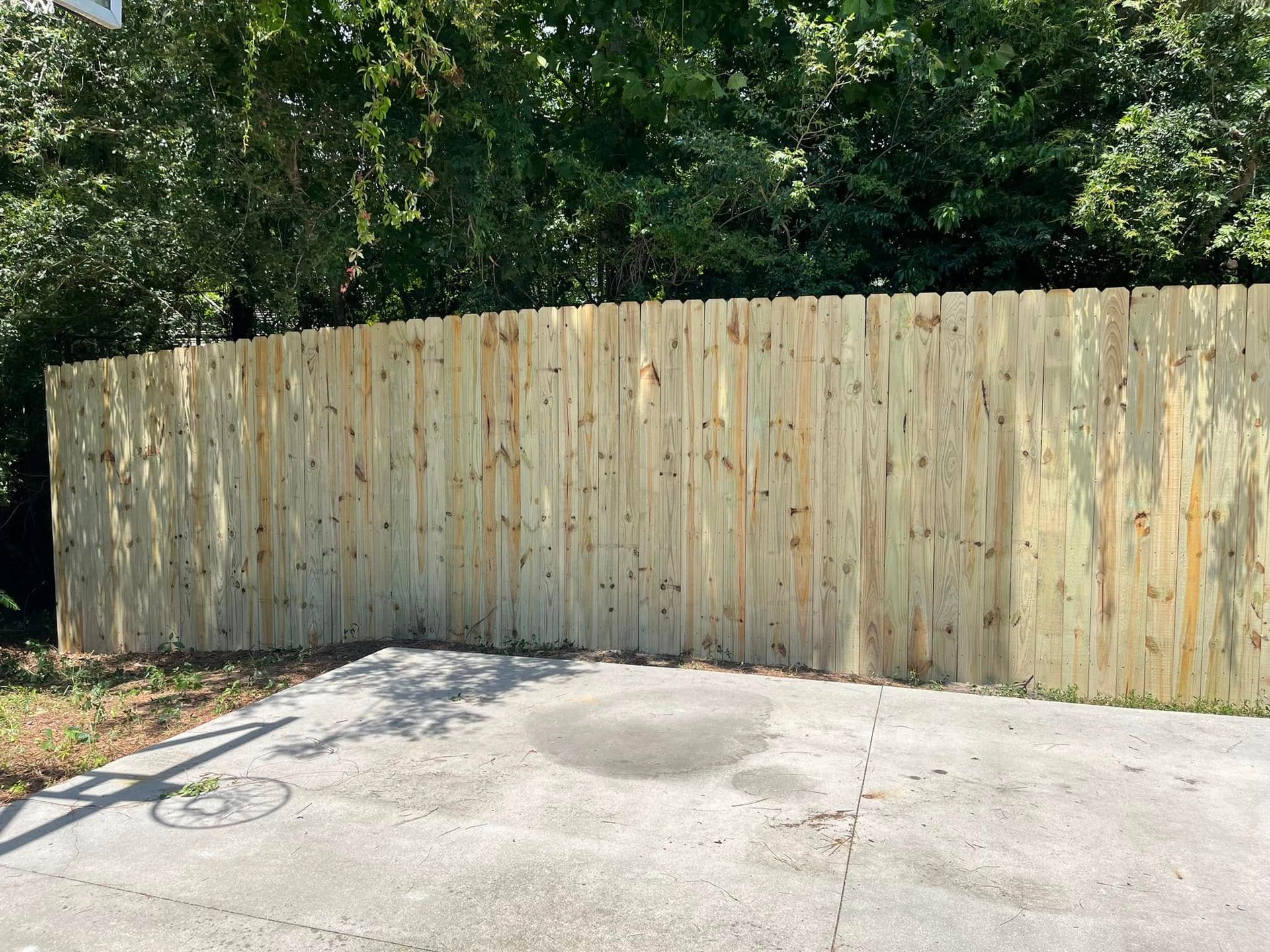 A wooden fence surrounds a parking lot with trees in the background.