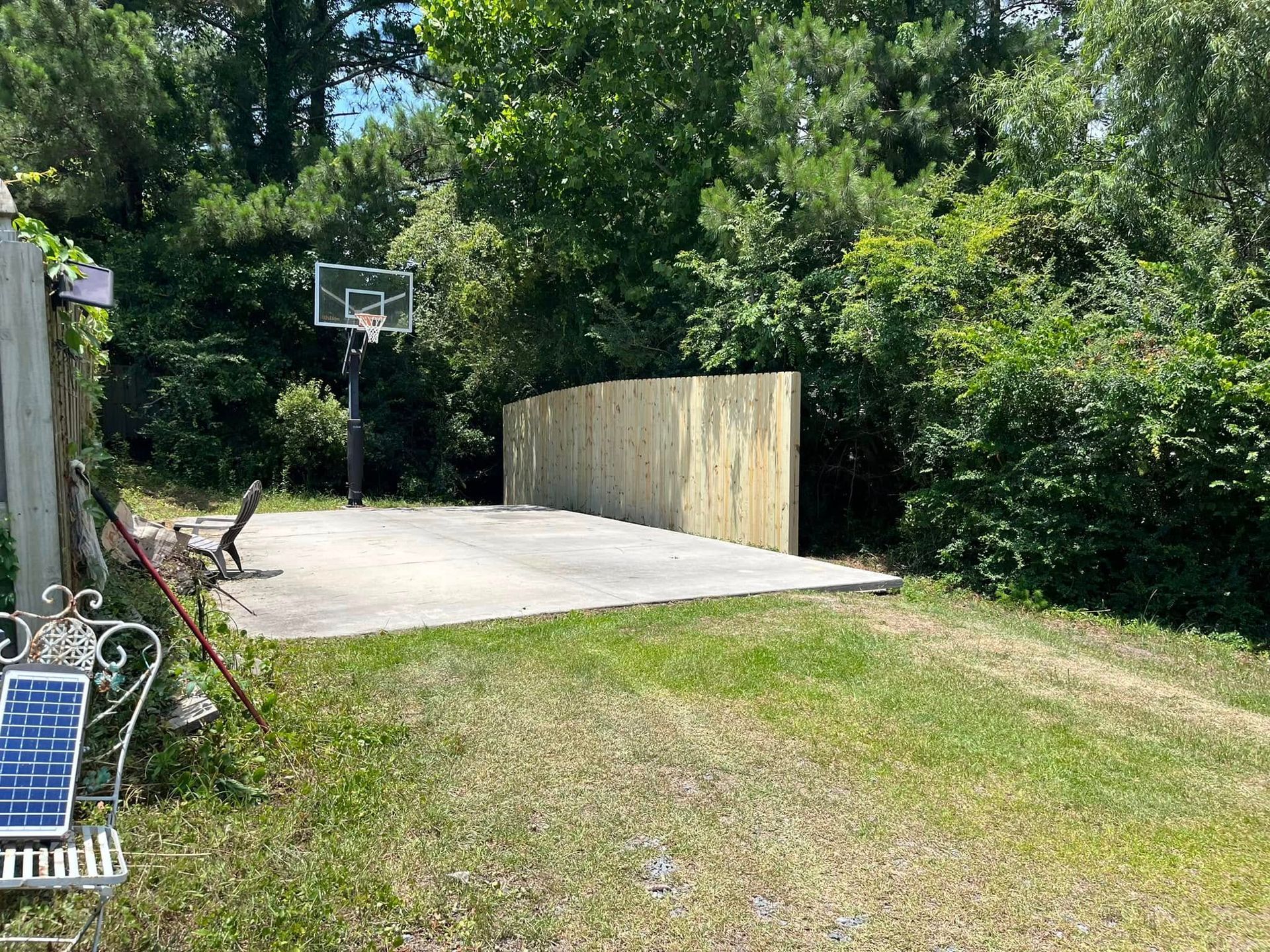 There is a basketball hoop in the backyard surrounded by trees.