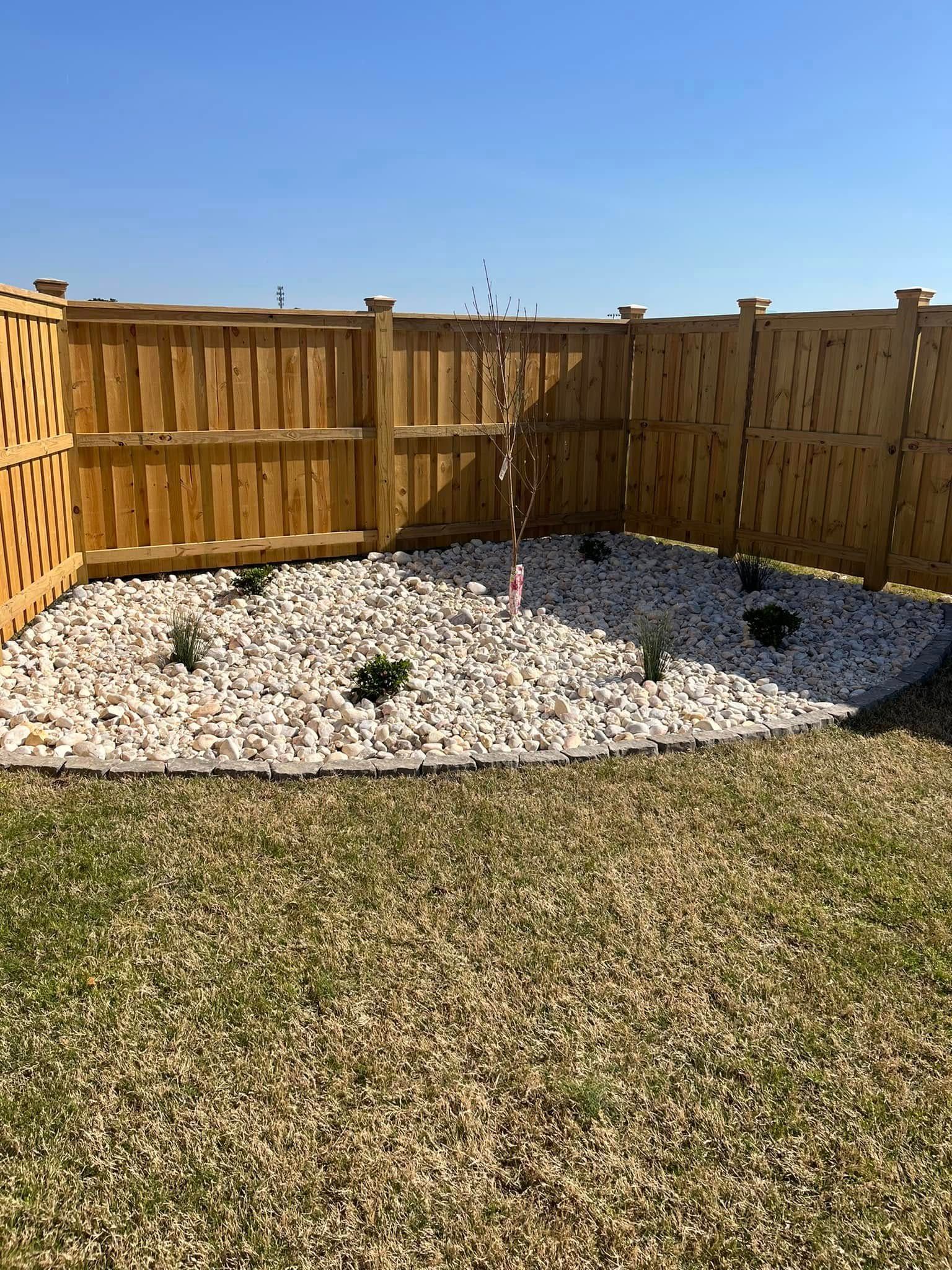 A wooden fence surrounds a gravel area in a backyard.