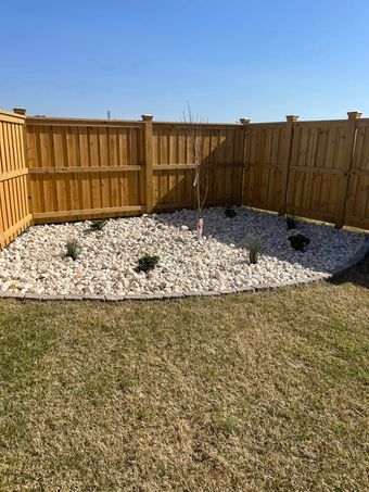 A wooden fence surrounds a gravel area in a backyard.