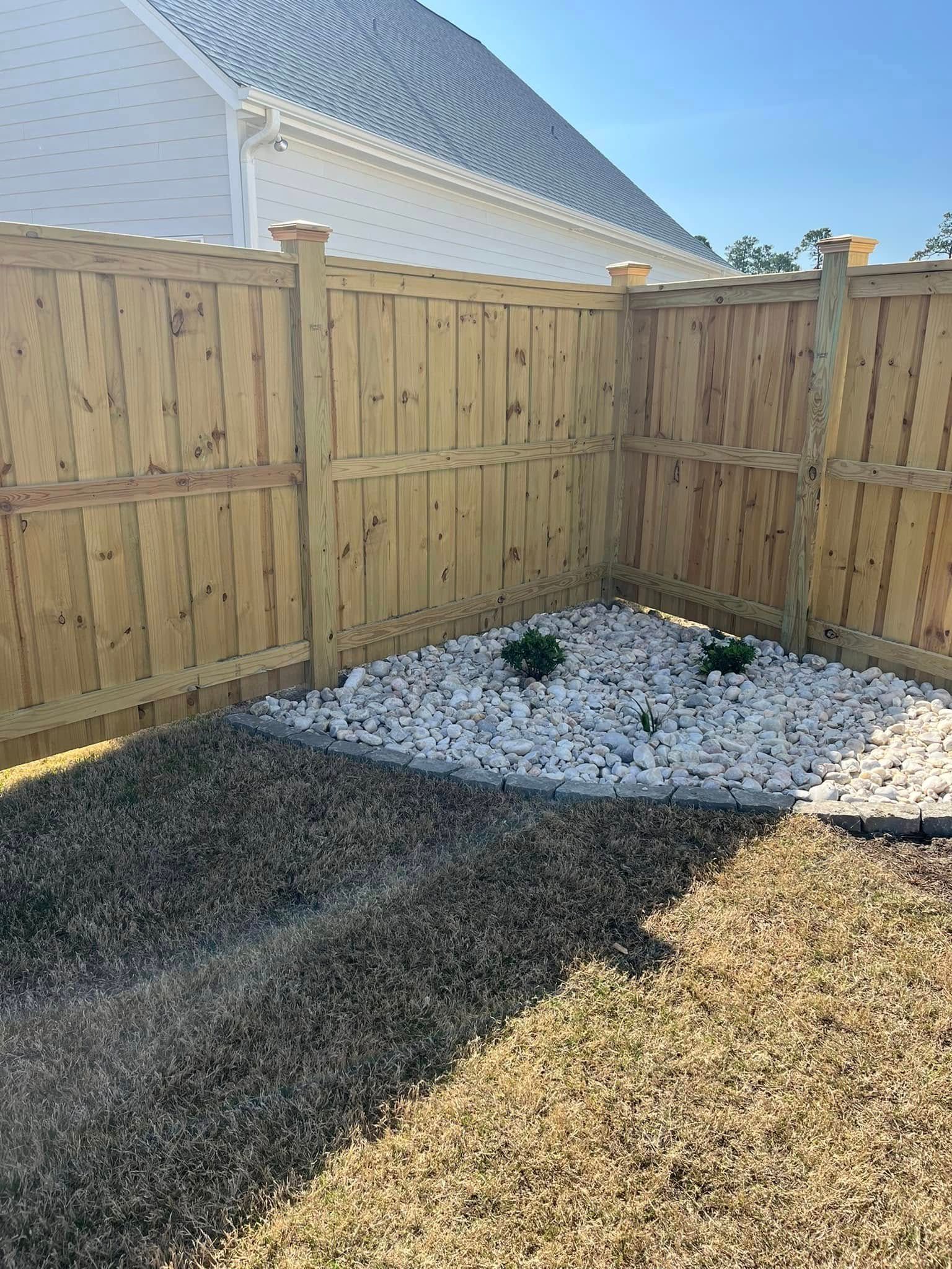 A wooden fence surrounds a gravel area in a backyard.