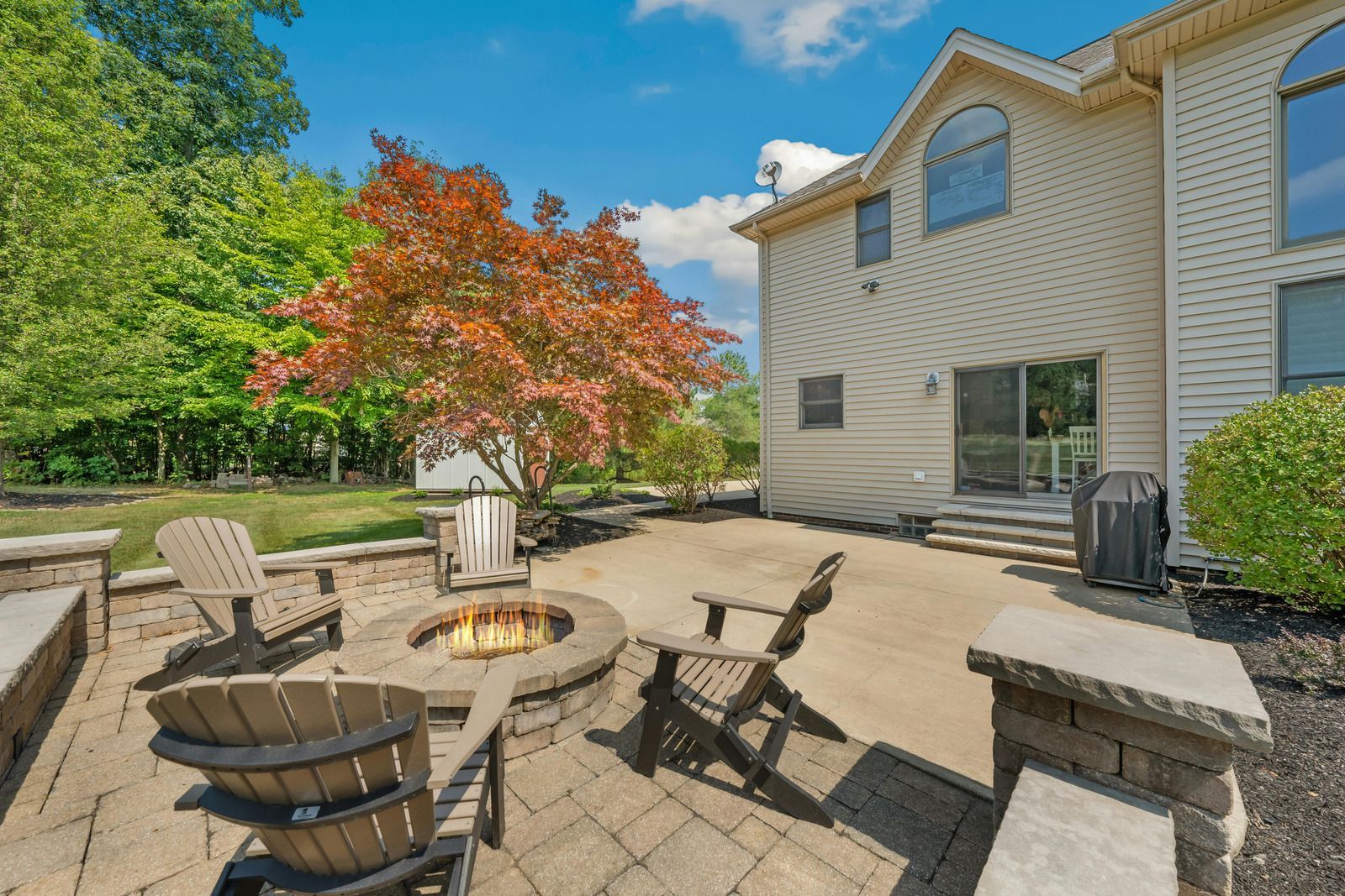 A patio with a fire pit and chairs in front of a house.