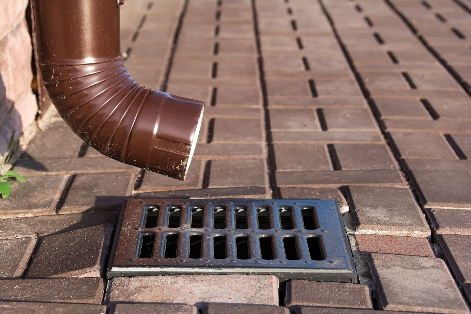 A brown drainpipe is connected to a drain on a brick sidewalk.